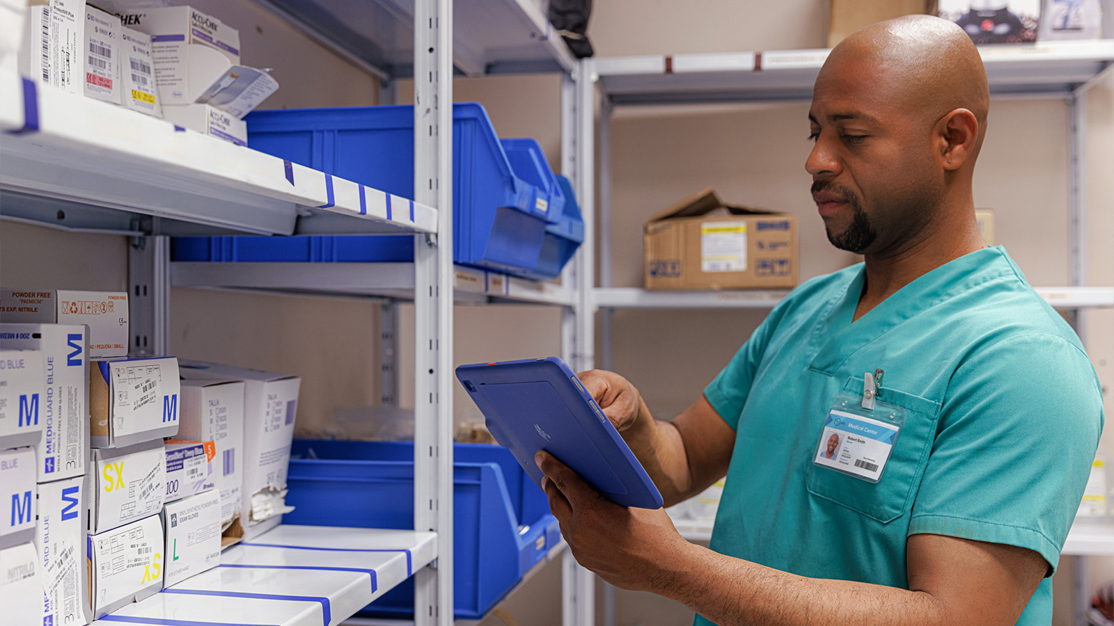 A healthcare professional is in a medical supply warehouse, holding a tablet and searching for information regarding the supplies.
