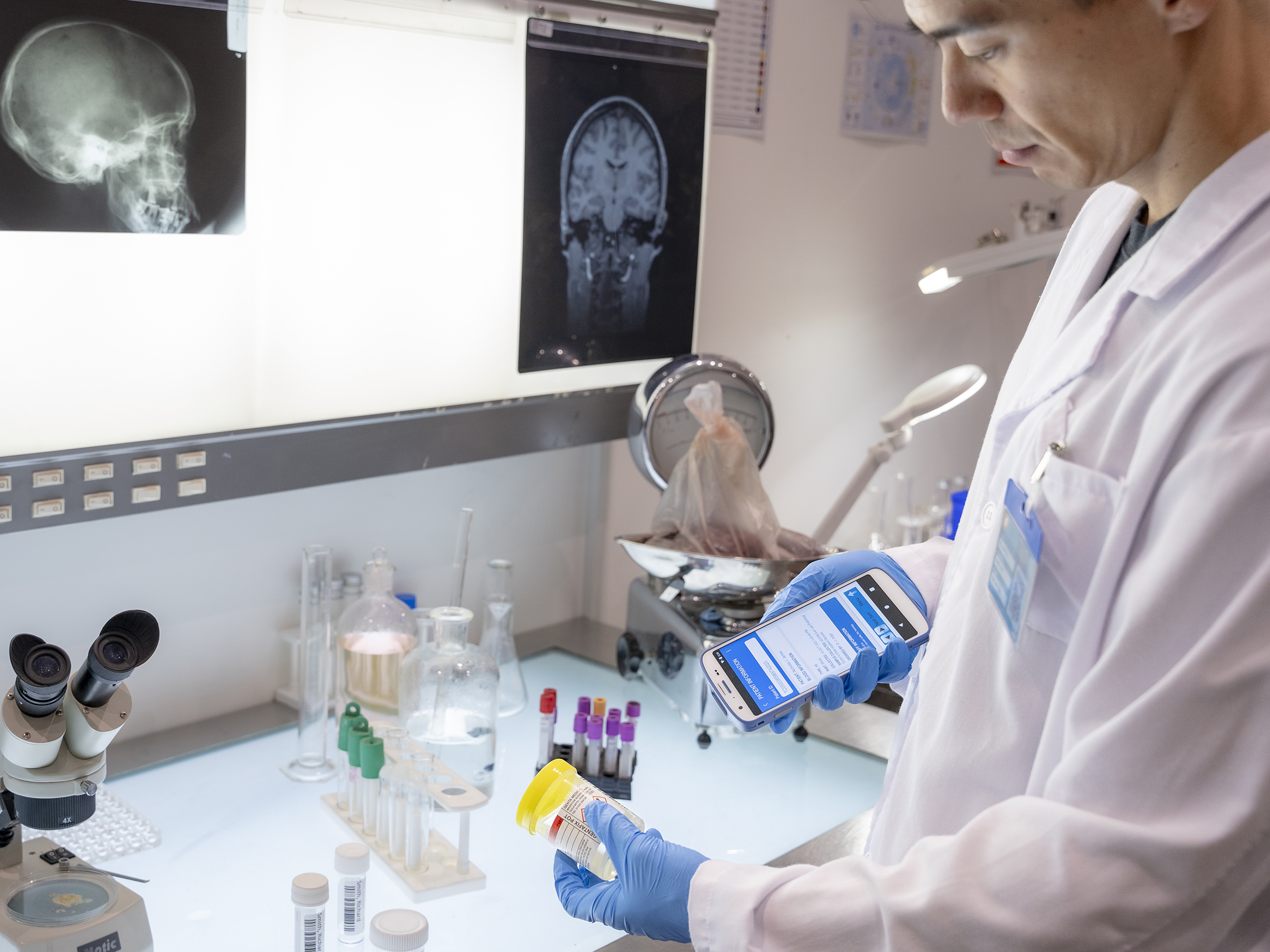 A healthcare employee uses a handheld mobile computer with an integrated scanner to identify a sample by scanning its container label.