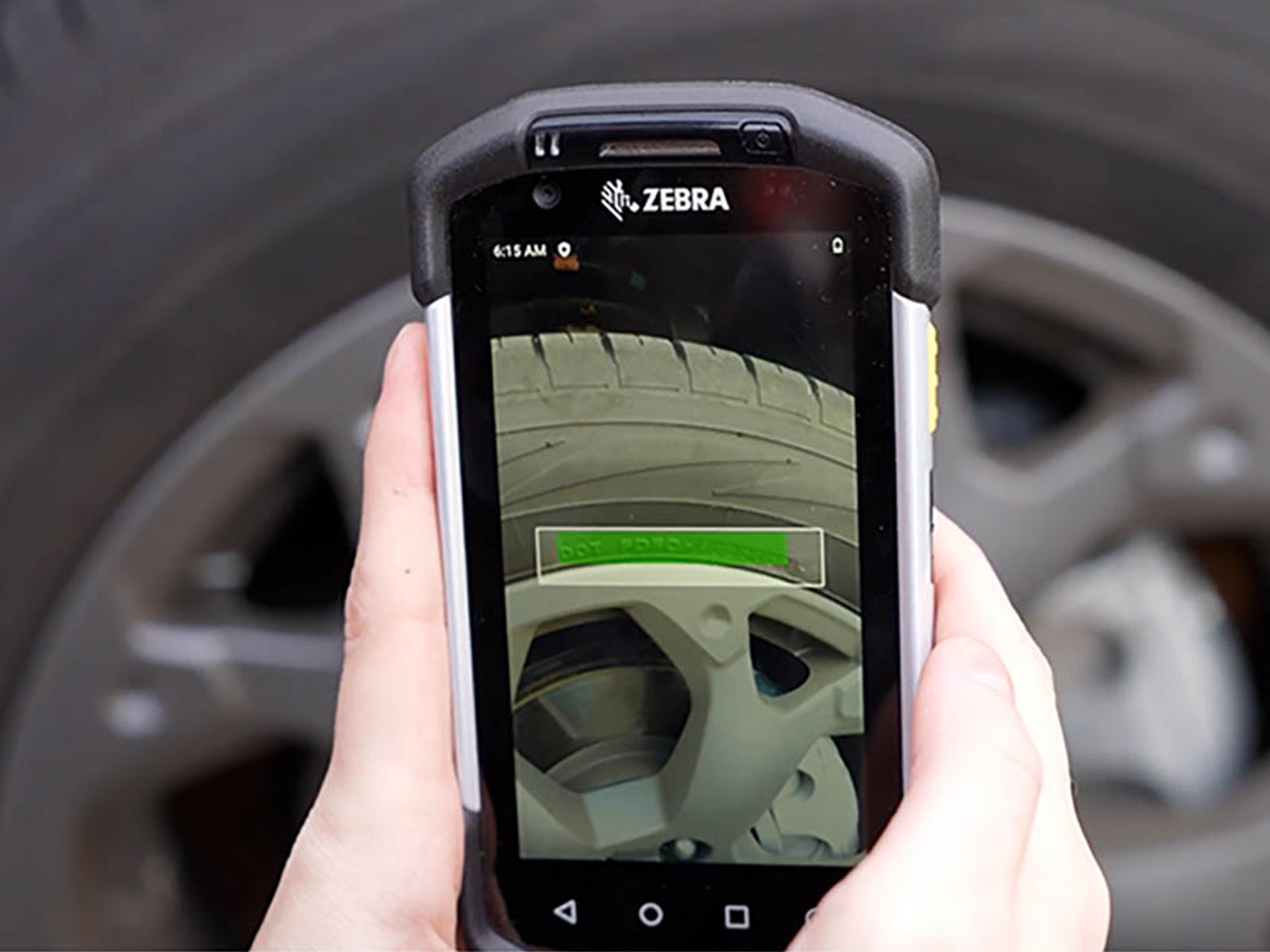 A person uses a Zebra handheld device with Optical Character Recognition OCR technology to scan and convert car tire tread patterns into machine-readable text for accurate documentation and analysis.