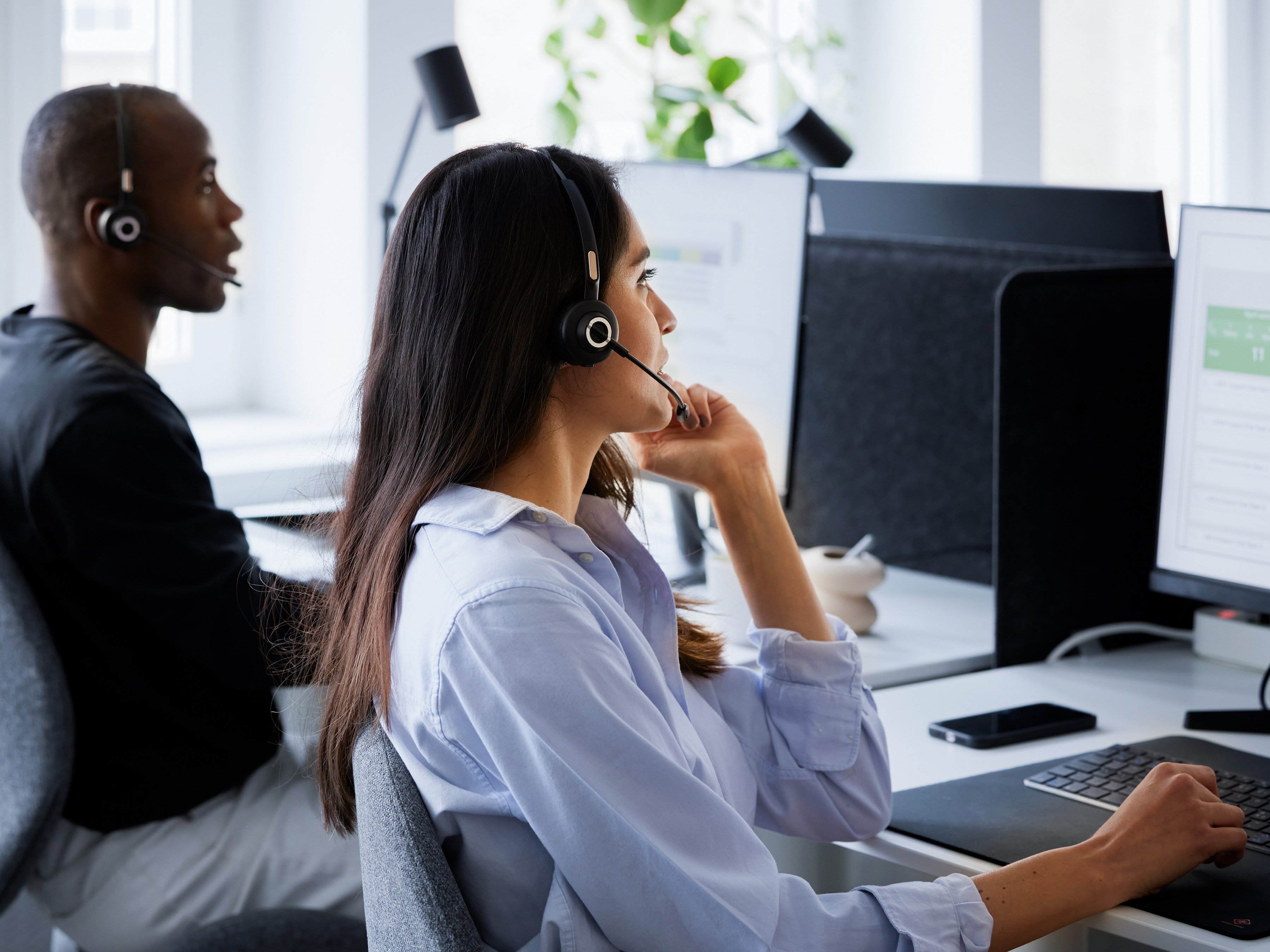 Two call center agents talking with customers at their workstations. Two call center agents talking with customers at their workstations.
