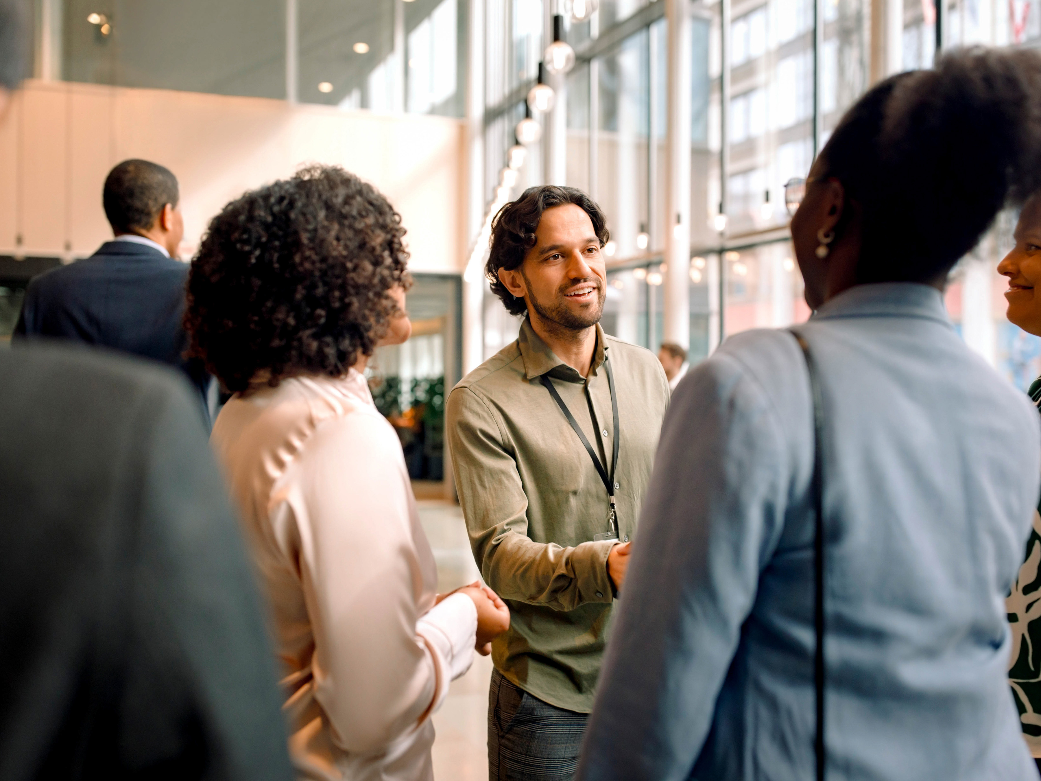 A group of professionals are meeting one another and exchanging handshakes at a conference center. A group of professionals are meeting one another and exchanging handshakes at a conference center.