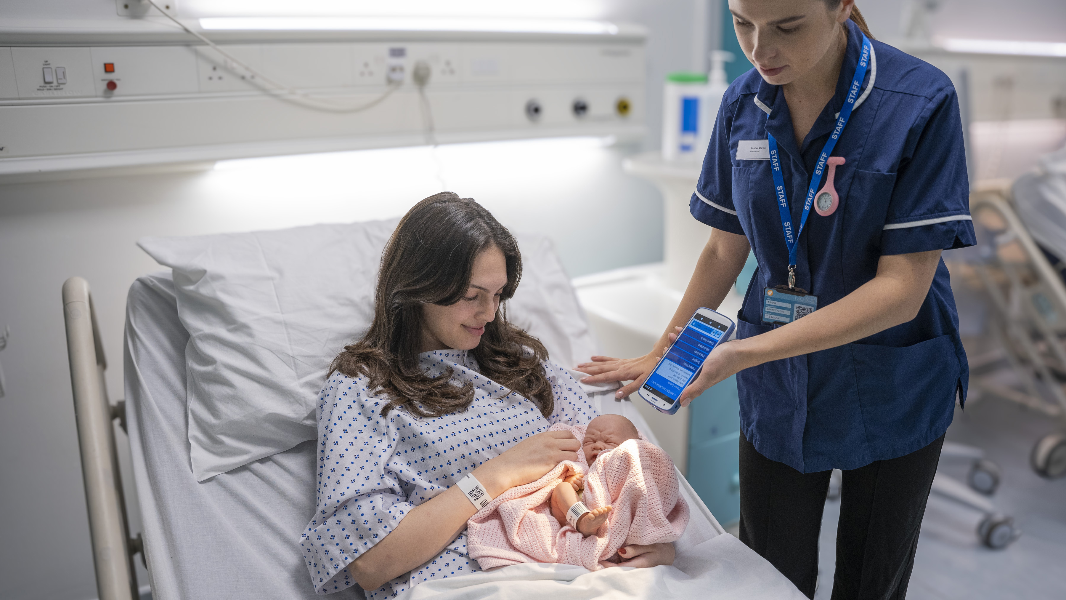 A mother holding her baby after giving birth at the hospital while the nurse is scanning her patient ID A mother holding her baby after giving birth at the hospital while the nurse is scanning her patient ID