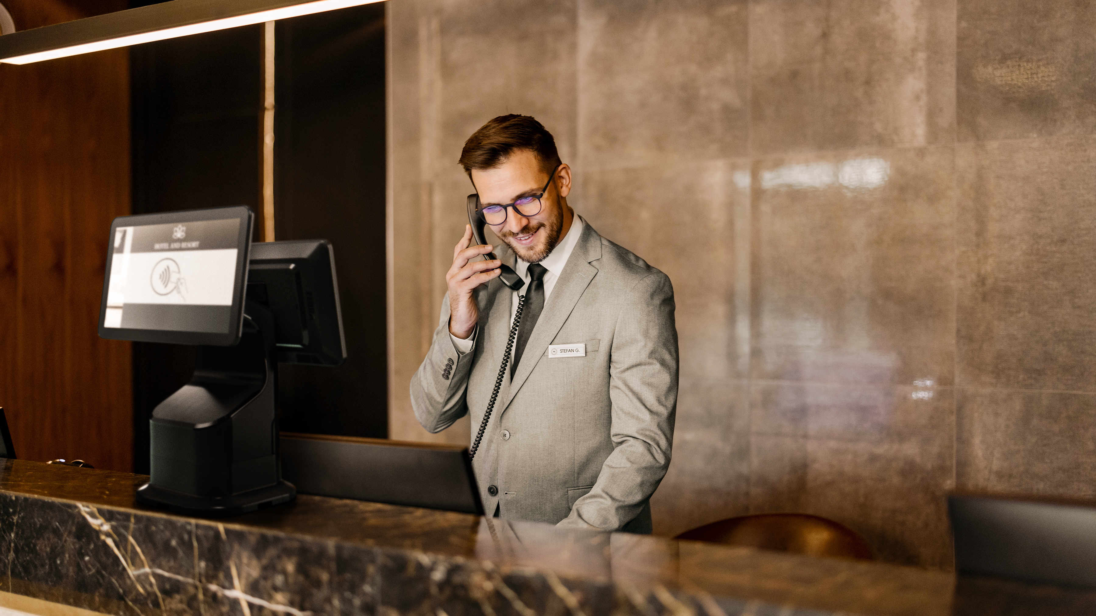 Hotel Desk attendant using a phone and a Zebra Interactive Kiosk. Hotel desk attendant using a phone and a Zebra Interactive Kiosk.