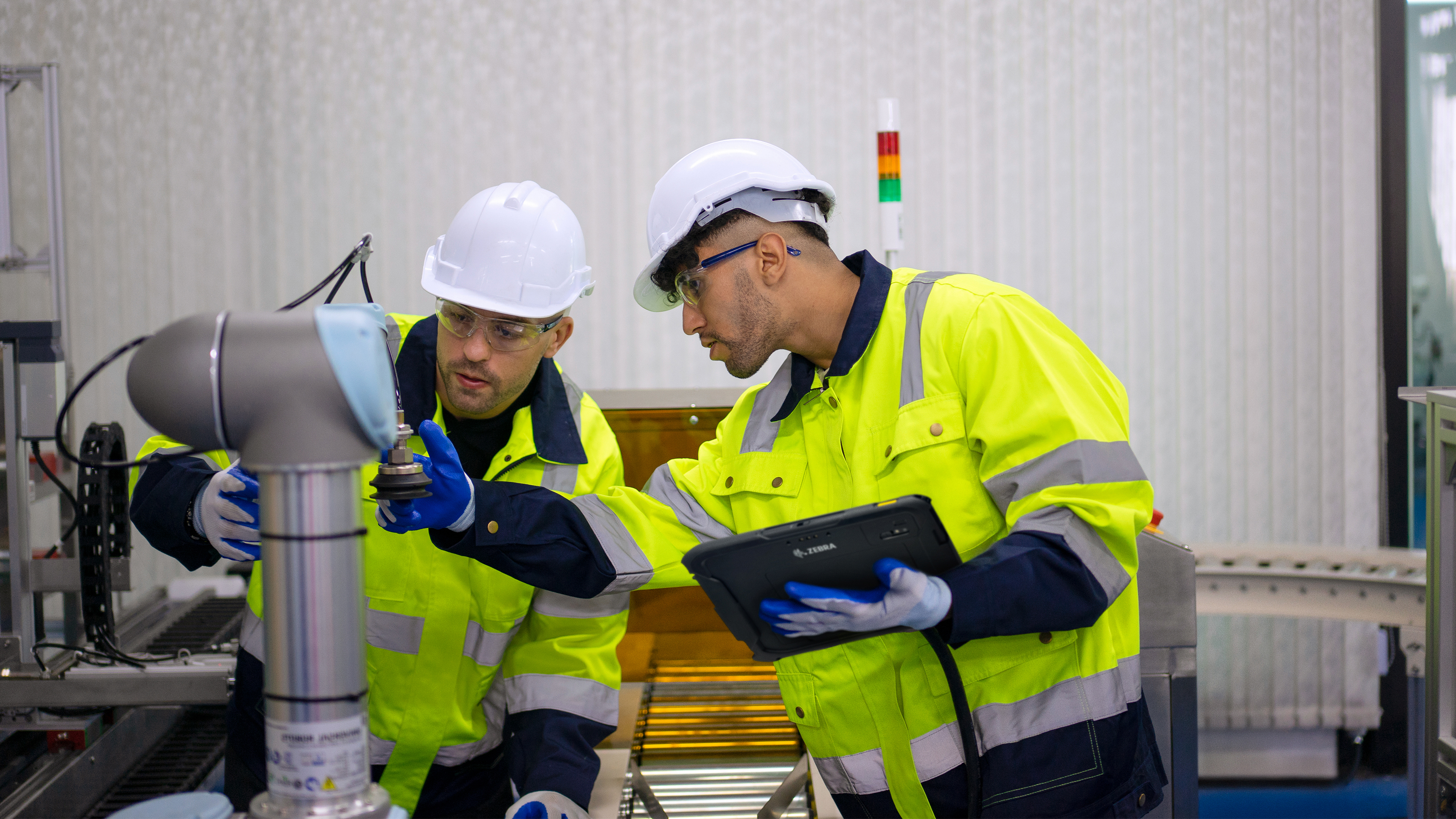 Two engineers configuring an industrial robotic arm using a Zebra tablet. Two engineers configuring an industrial robotic arm using a Zebra tablet.