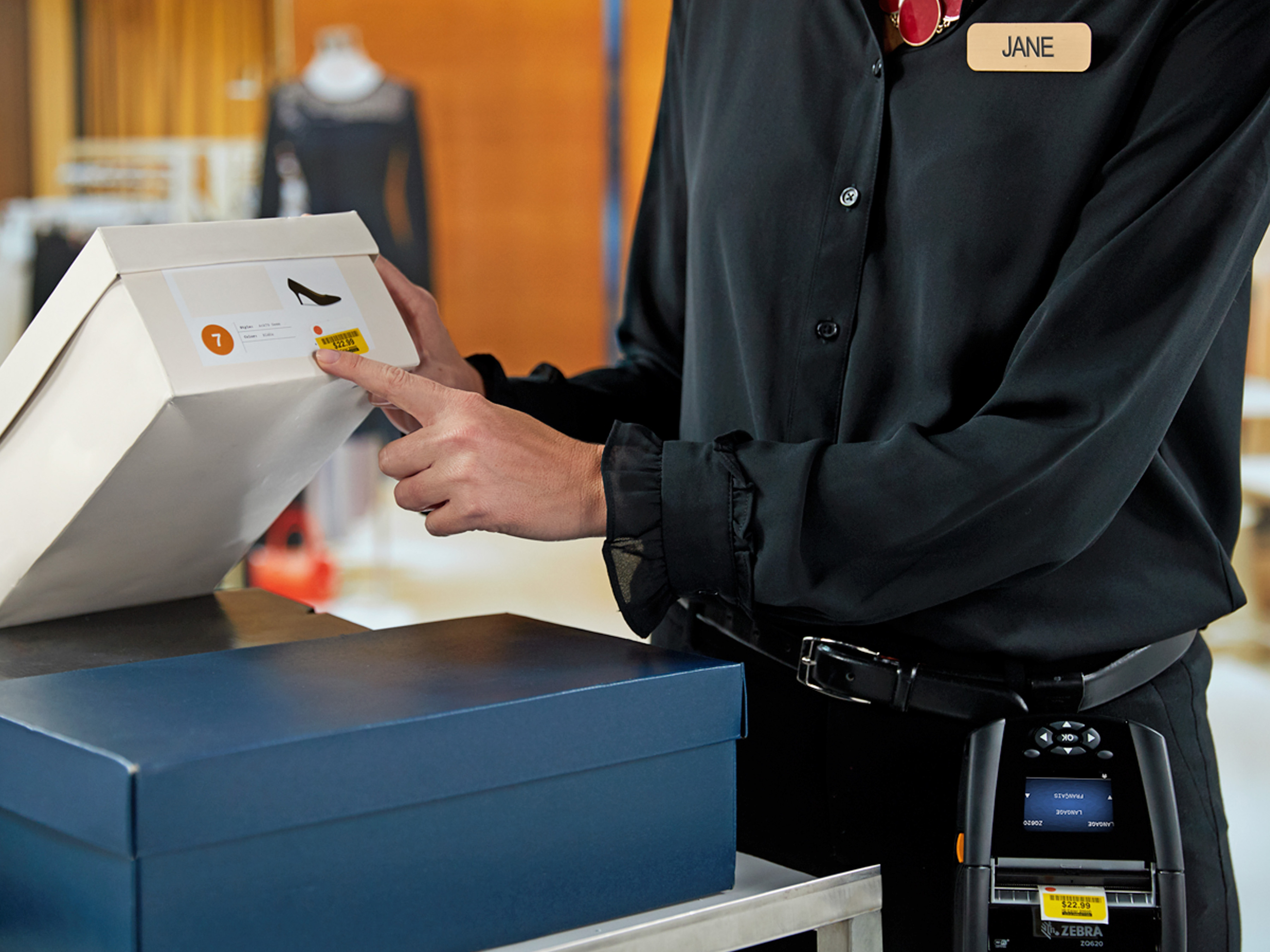 Retail worker applying a label to a shoe box using a Zebra Mobile Printer. Retail worker applying a label to a shoe box using a Zebra Mobile Printer.