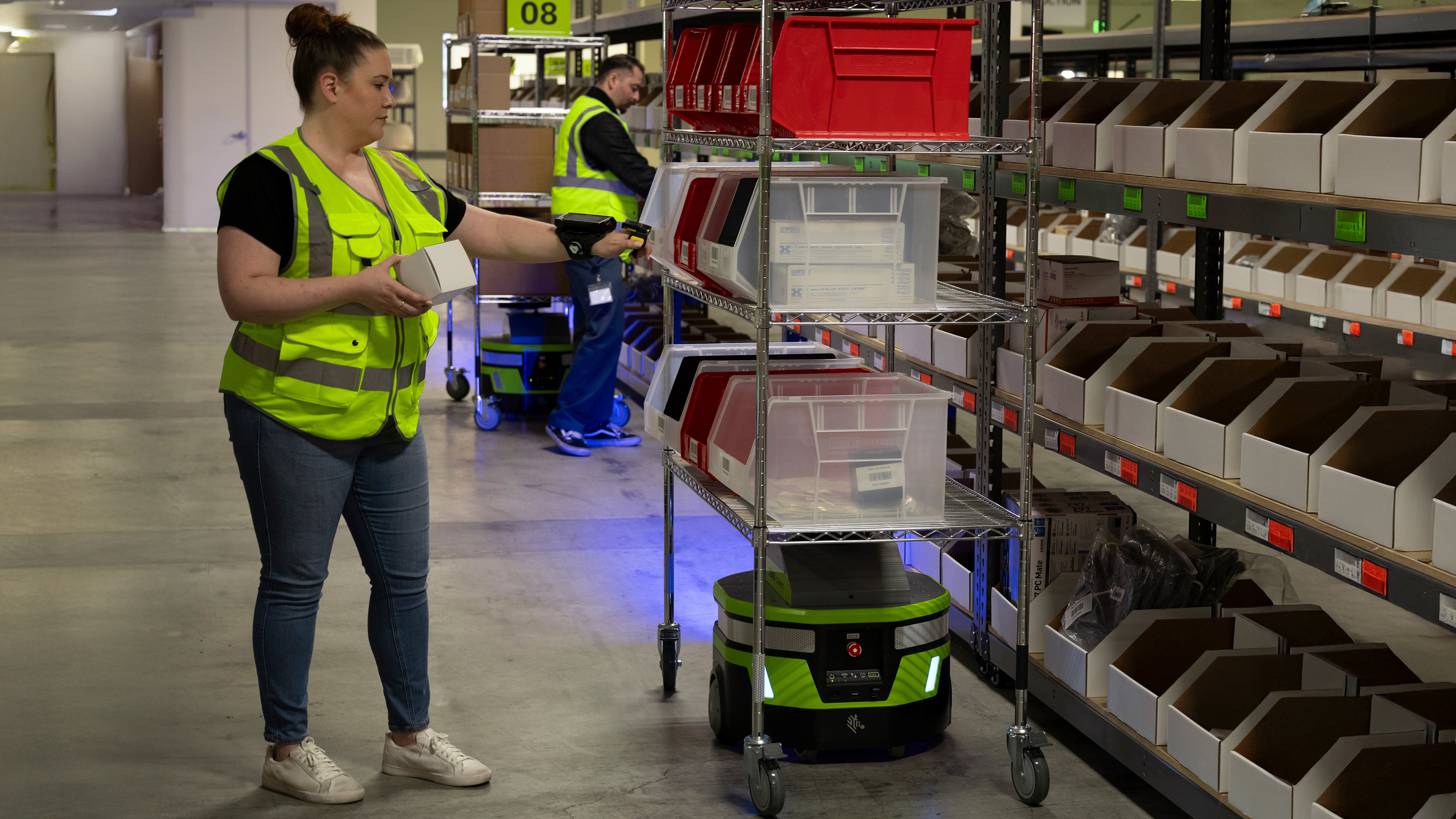 Warehouse staff holding a white box in front of the shelves and Zebra mobile robot Warehouse staff holding a white box in front of the shelves and Zebra mobile robot