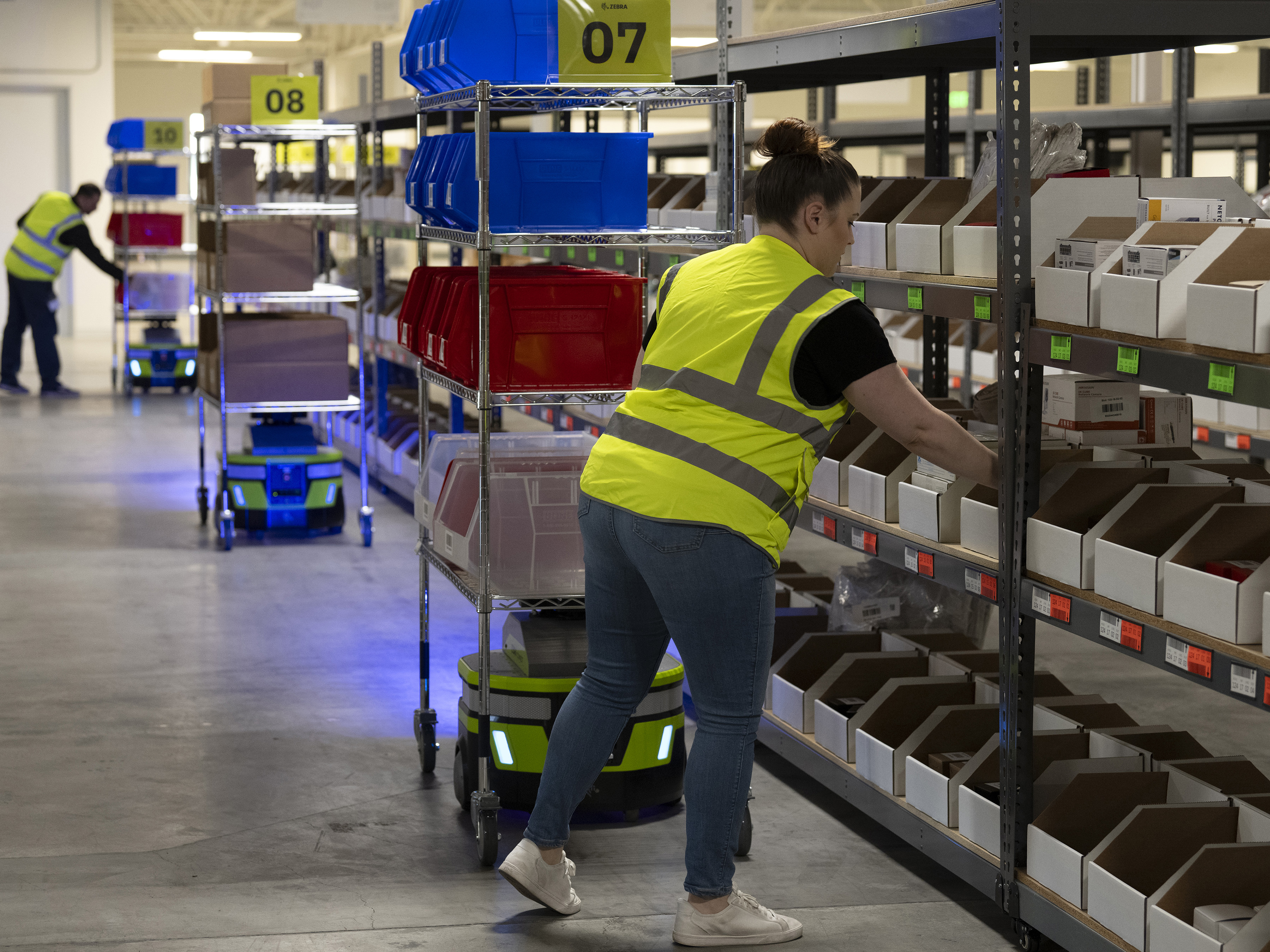 Warehouse workers organizing the shelves with Zebra mobile robots Warehouse workers organizing the shelves with Zebra mobile robots