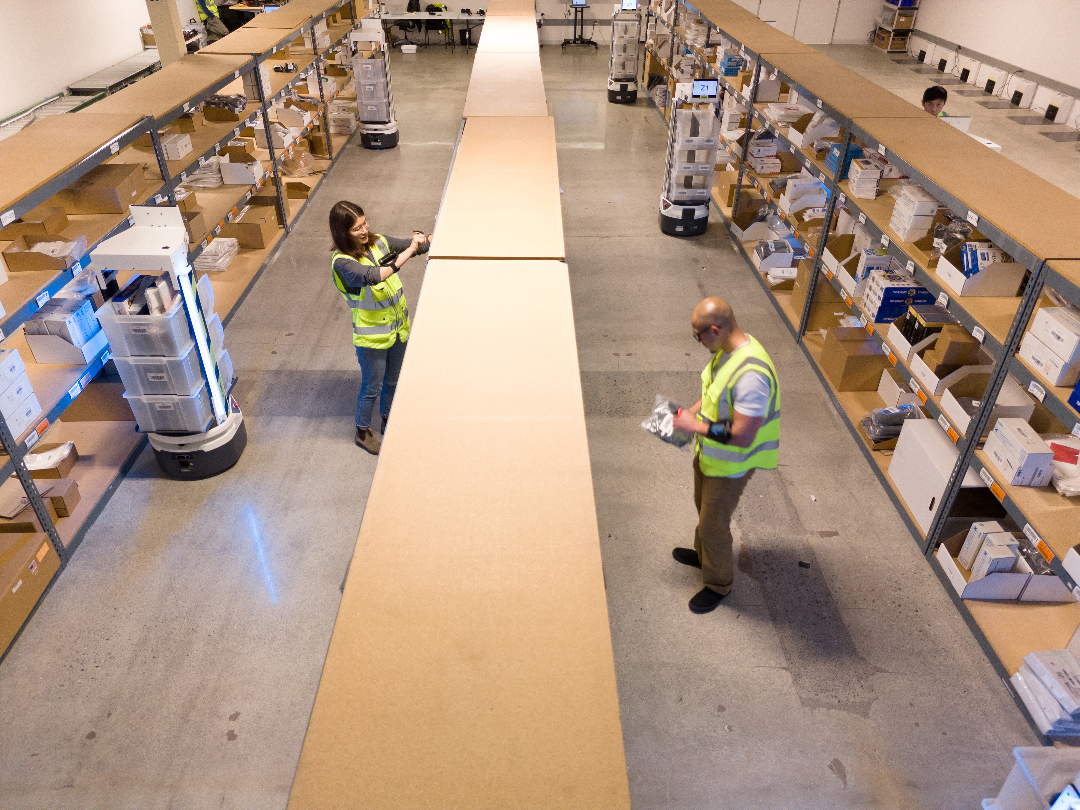 Two workers and Zebra mobile robots inside a warehouse Two workers and Zebra mobile robots inside a warehouse