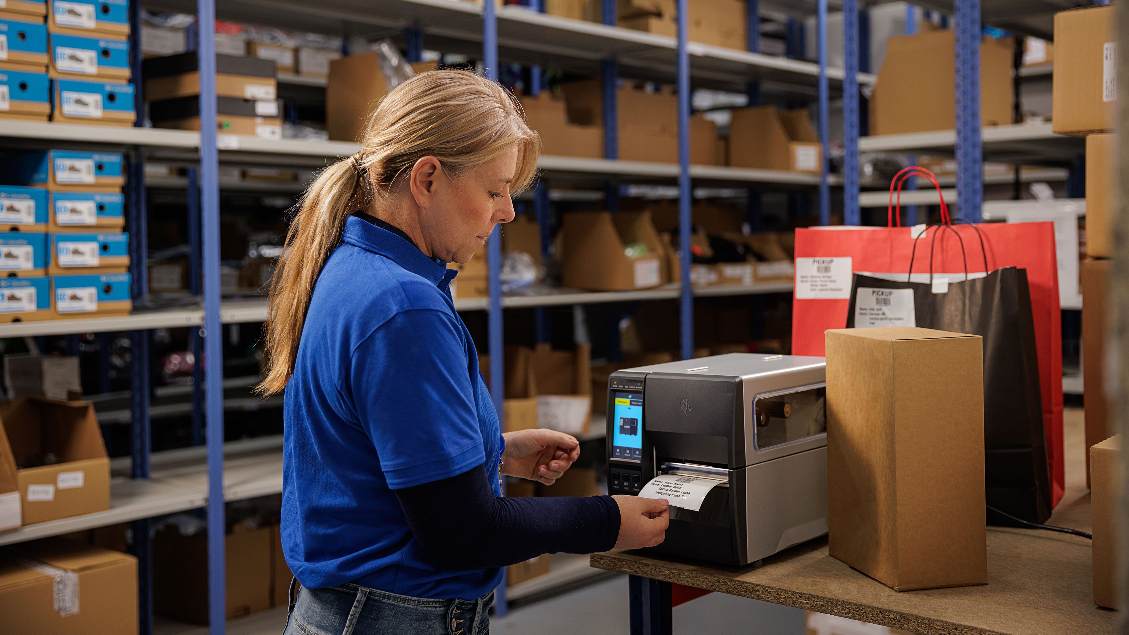 Warehouse working printing a label using a Zebra industrial printer in a stockroom. Warehouse working printing a label using a Zebra industrial printer in a stockroom.