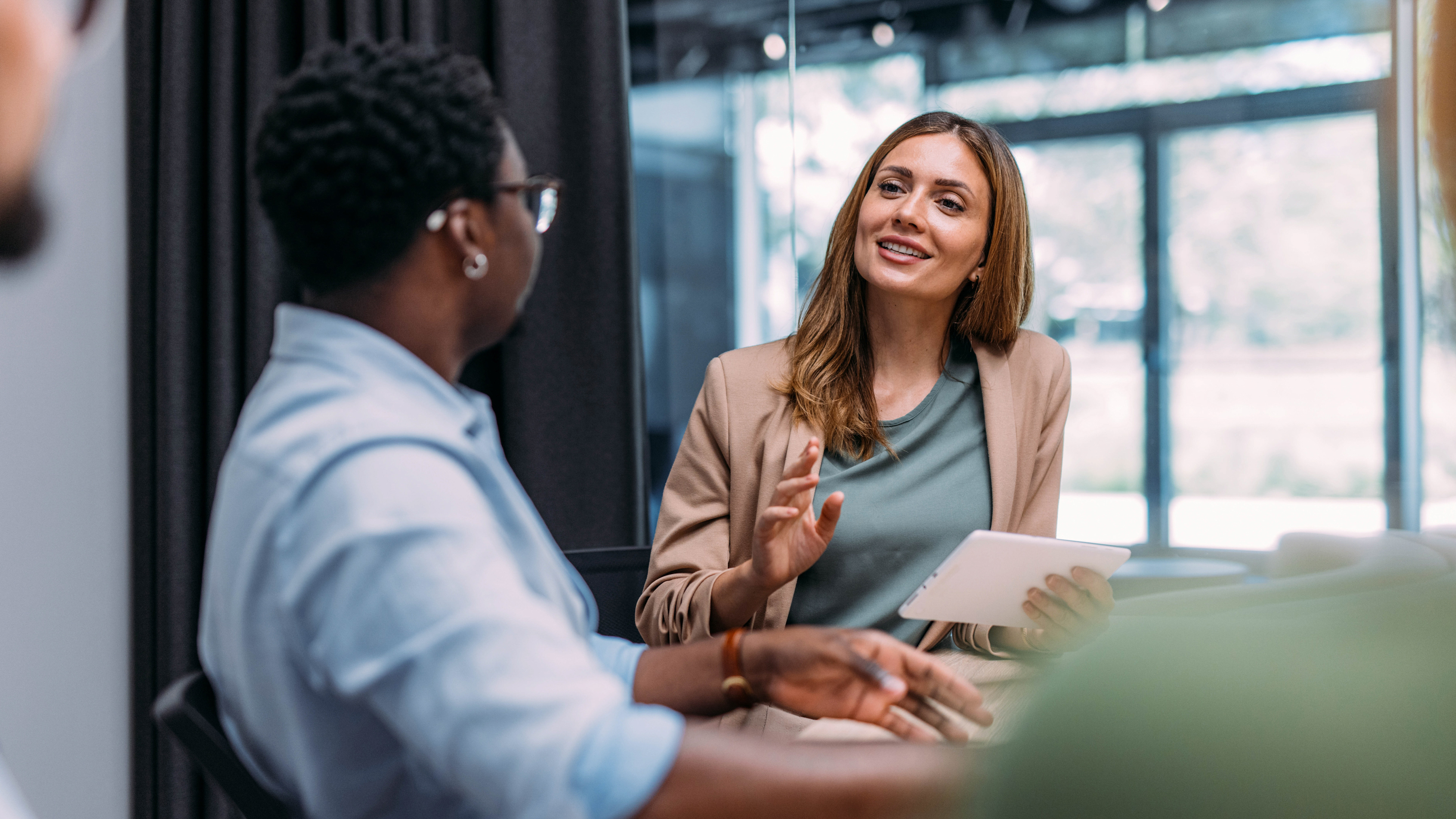 A business professional is holding a tablet while talking to colleagues at a conference table in the office. A business professional is holding a tablet while talking to colleagues at a conference table in the office.