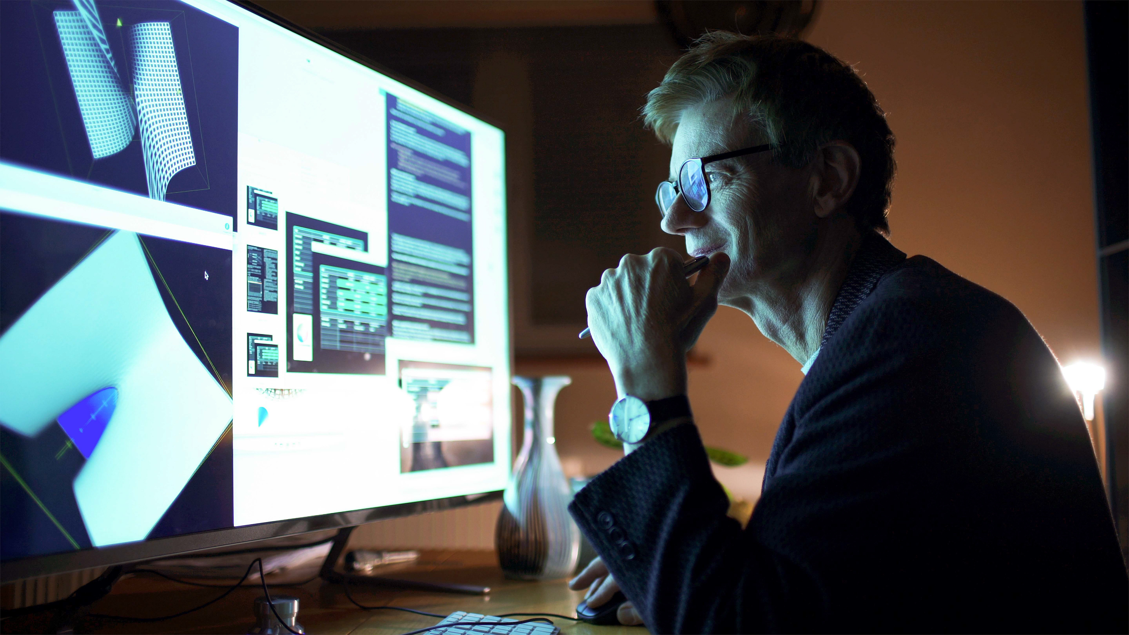 An employee works late into the night at a desktop computer, where a large monitor displays a various image models and code. An employee works late into the night at a desktop computer, where a large monitor displays a various image models and code.