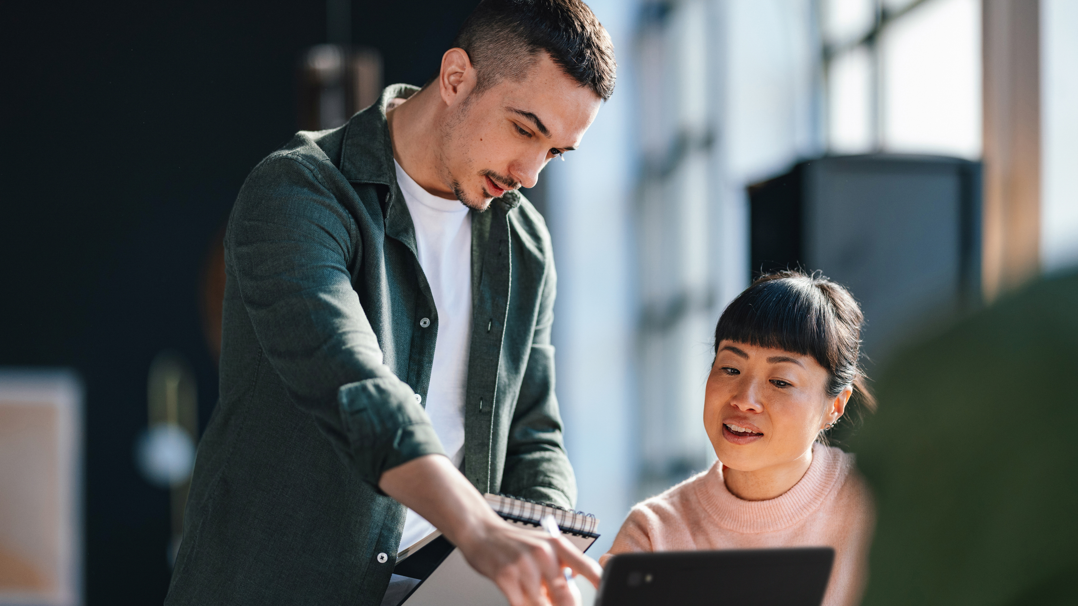 Two employees reviewing a laptop while working together in an office. Two employees reviewing a laptop while working together in an office.