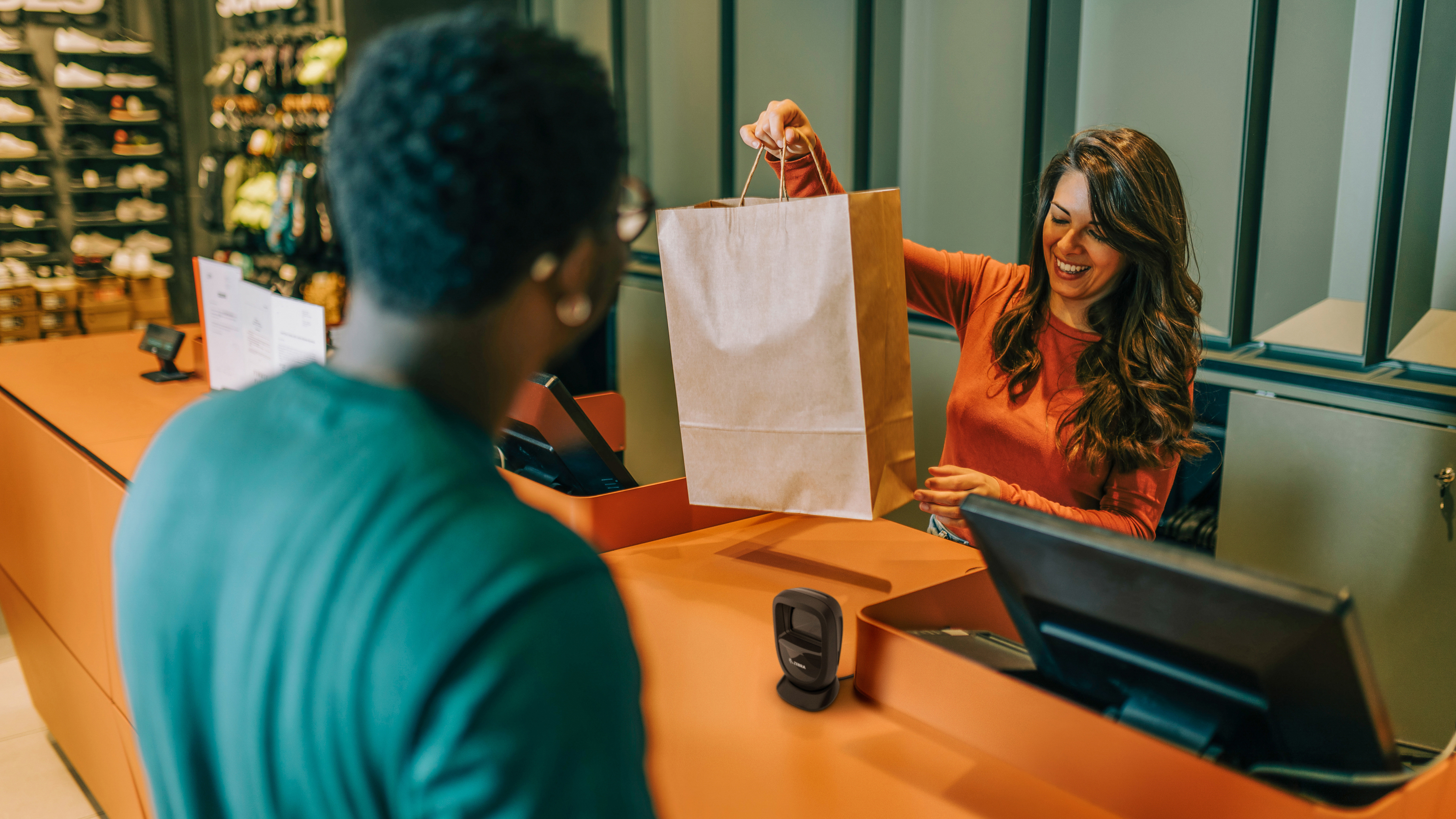 An employee handing a shopper their purchase at the checkout of a shoe store. An employee handing a shopper their purchase at the checkout of a shoe store.