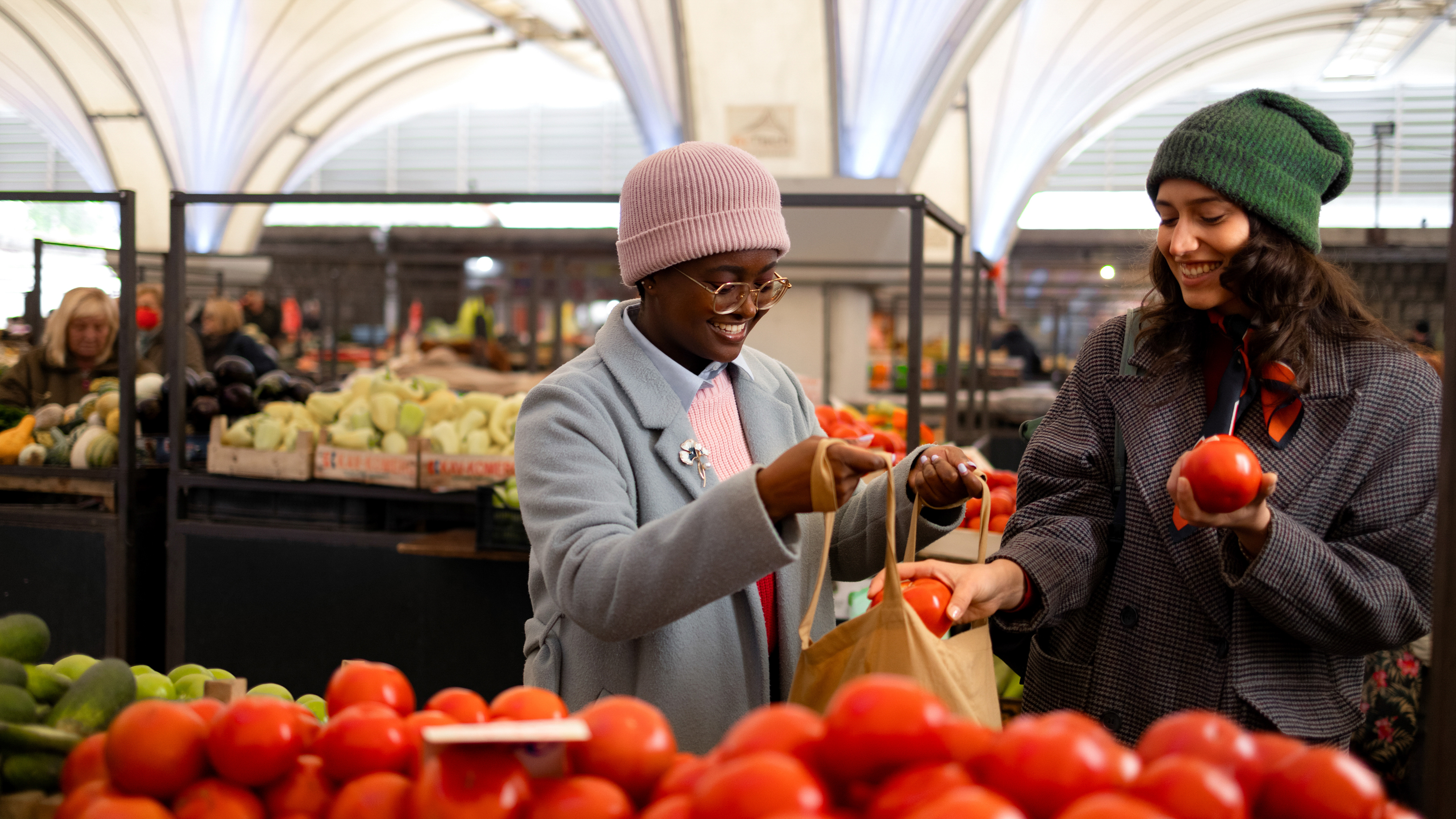 Two shoppers selecting tomatoes inside a grocery store produce department. Two shoppers selecting tomatoes inside a grocery store produce department.