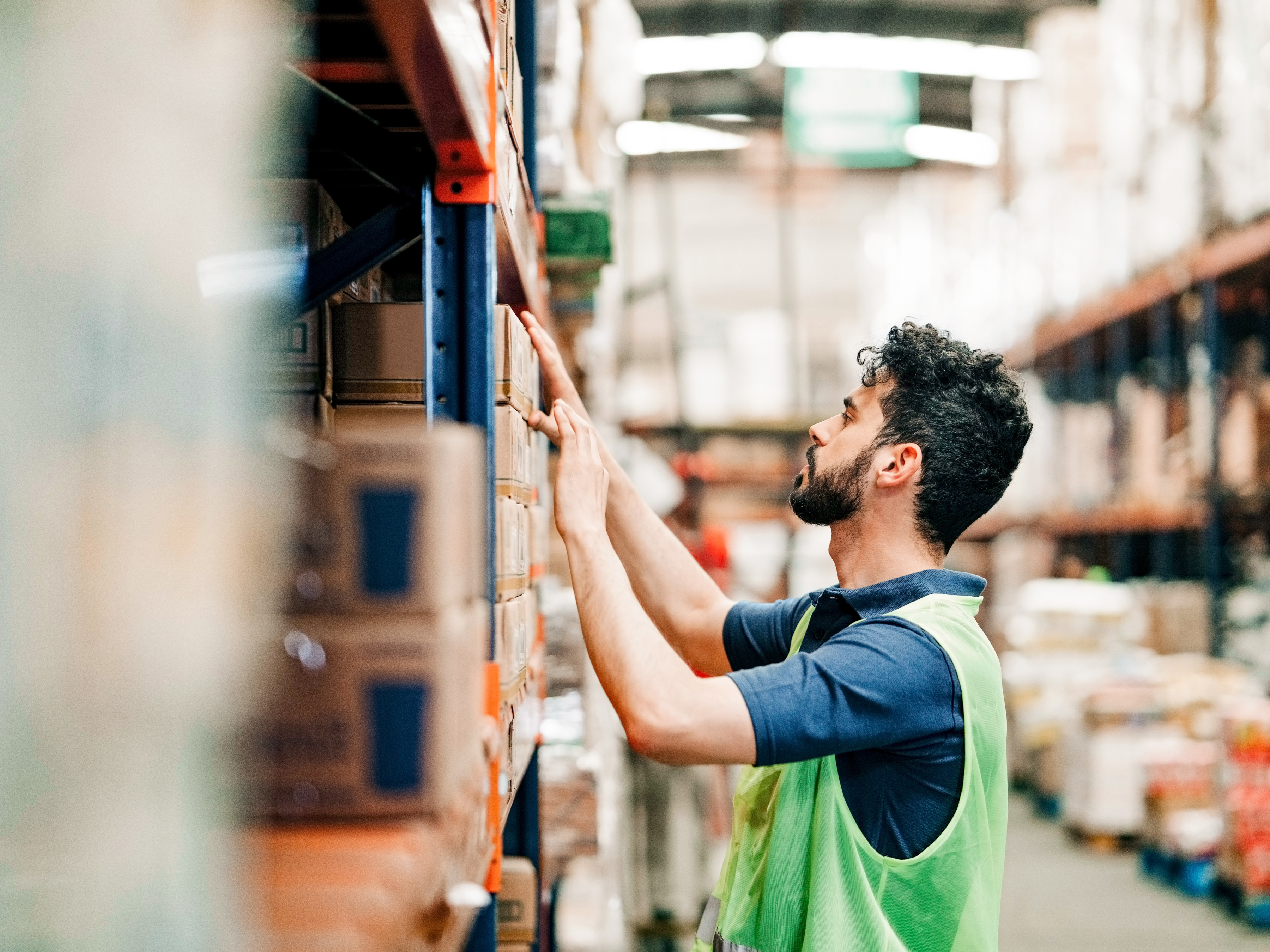 A worker is checking inventory on a shelf in a warehouse. A worker is checking inventory on a shelf in a warehouse.
