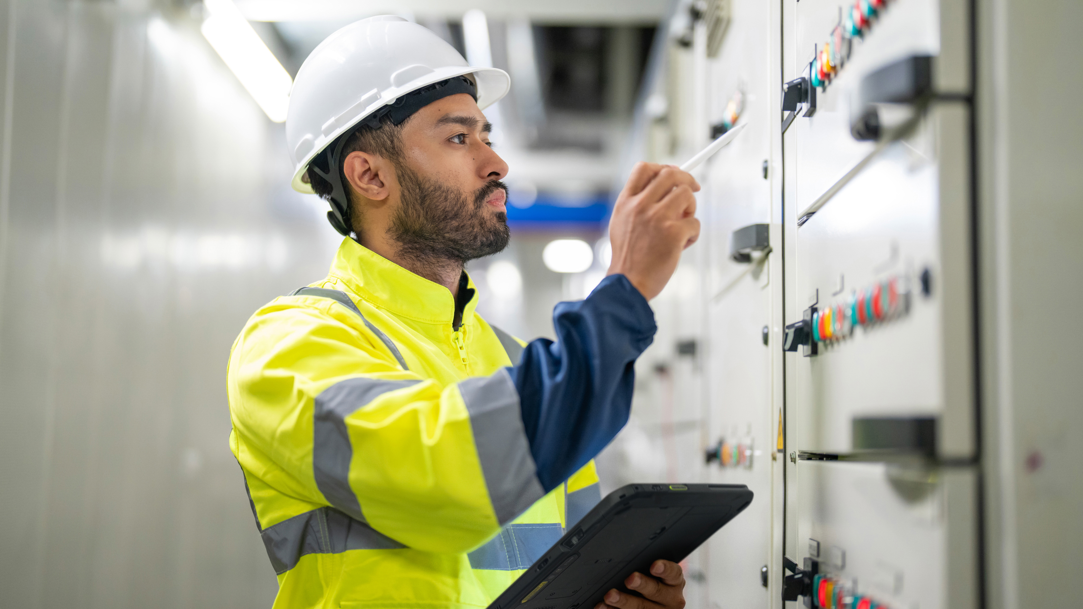 An engineer inspecting a control panel inside of an industrial facility. An engineer inspecting a control panel inside of an industrial facility.