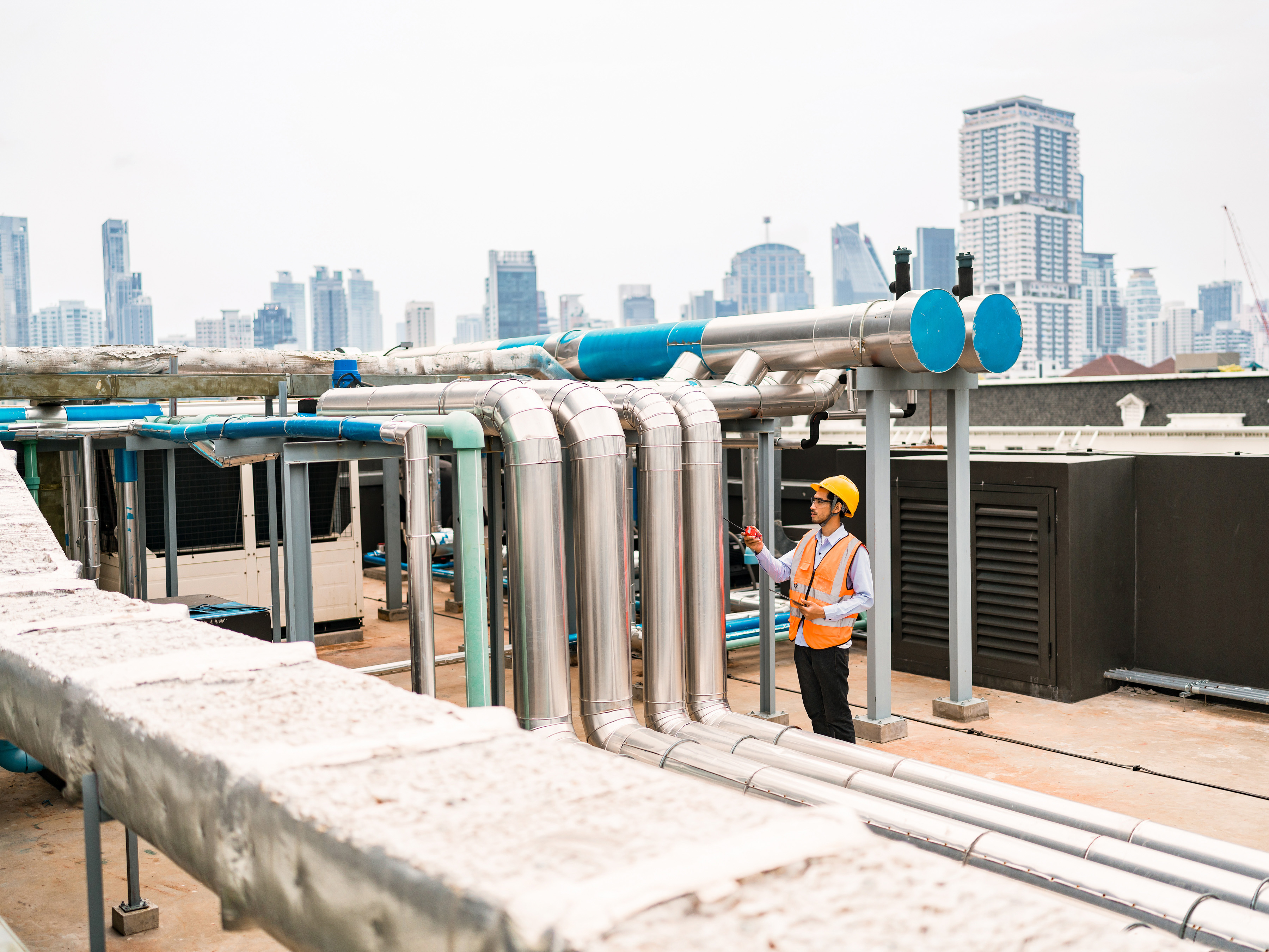 Engineer inspecting industrial piping on the roof of a city building.  Engineer inspecting industrial piping on the roof of a city building.