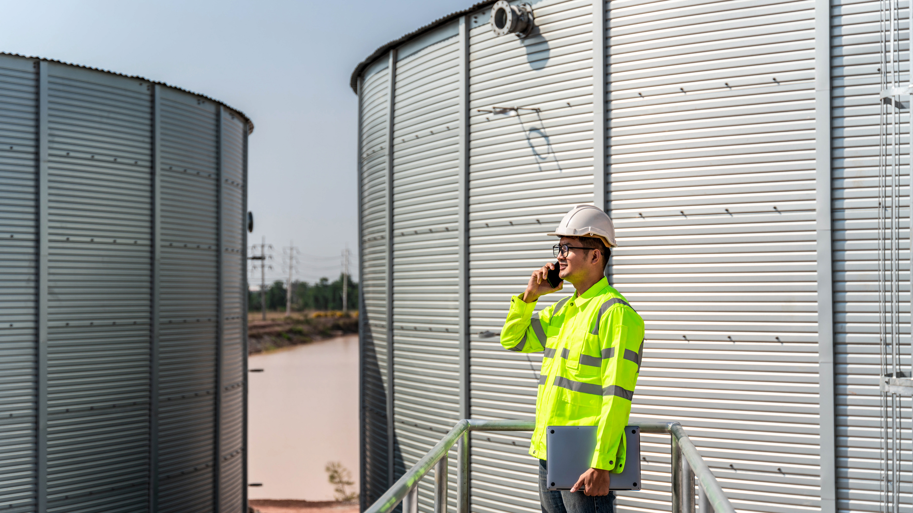 An industrial worker on a phone call using a mobile computer holding a laptop at a production site. An industrial worker on a phone call using a mobile computer holding a laptop at a production site.