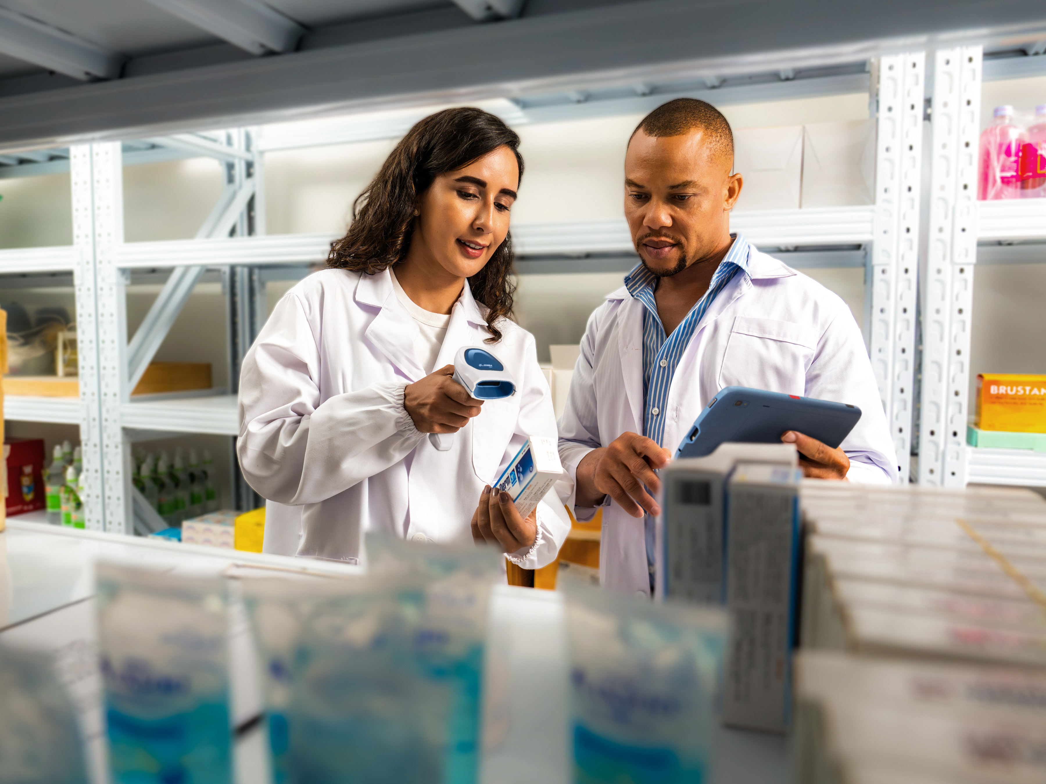 A medical professional uses a Zebra handheld barcode scanner to scan a label on a prescription medication while their colleague with a Zebra tablet watches. A medical professional uses a Zebra handheld barcode scanner to scan a label on a prescription medication while their colleague with a Zebra tablet watches.