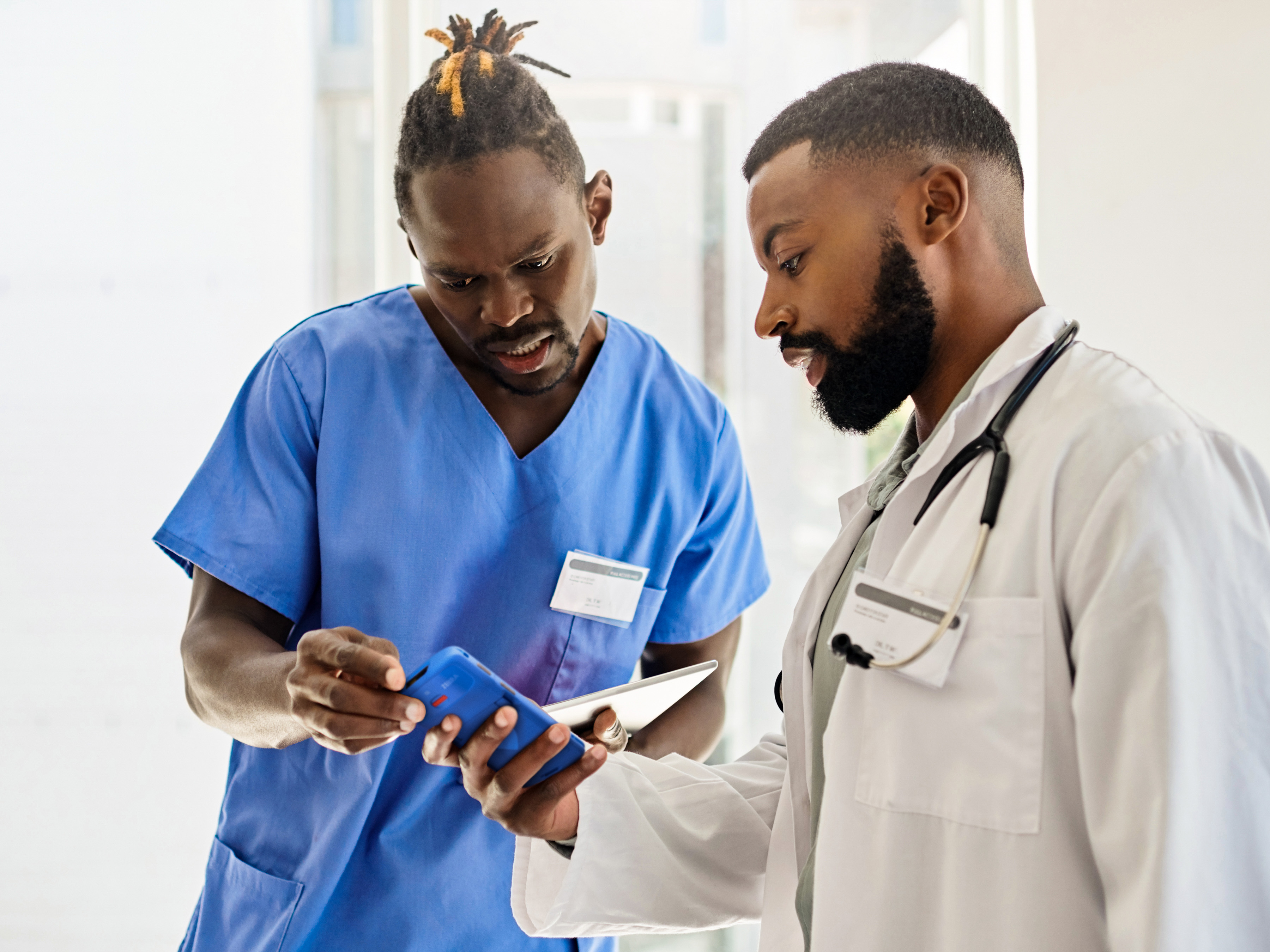 Two medical professionals reviewing a Zebra handheld mobile computer inside of a hospital. Two medical professionals reviewing a Zebra handheld mobile computer inside of a hospital.