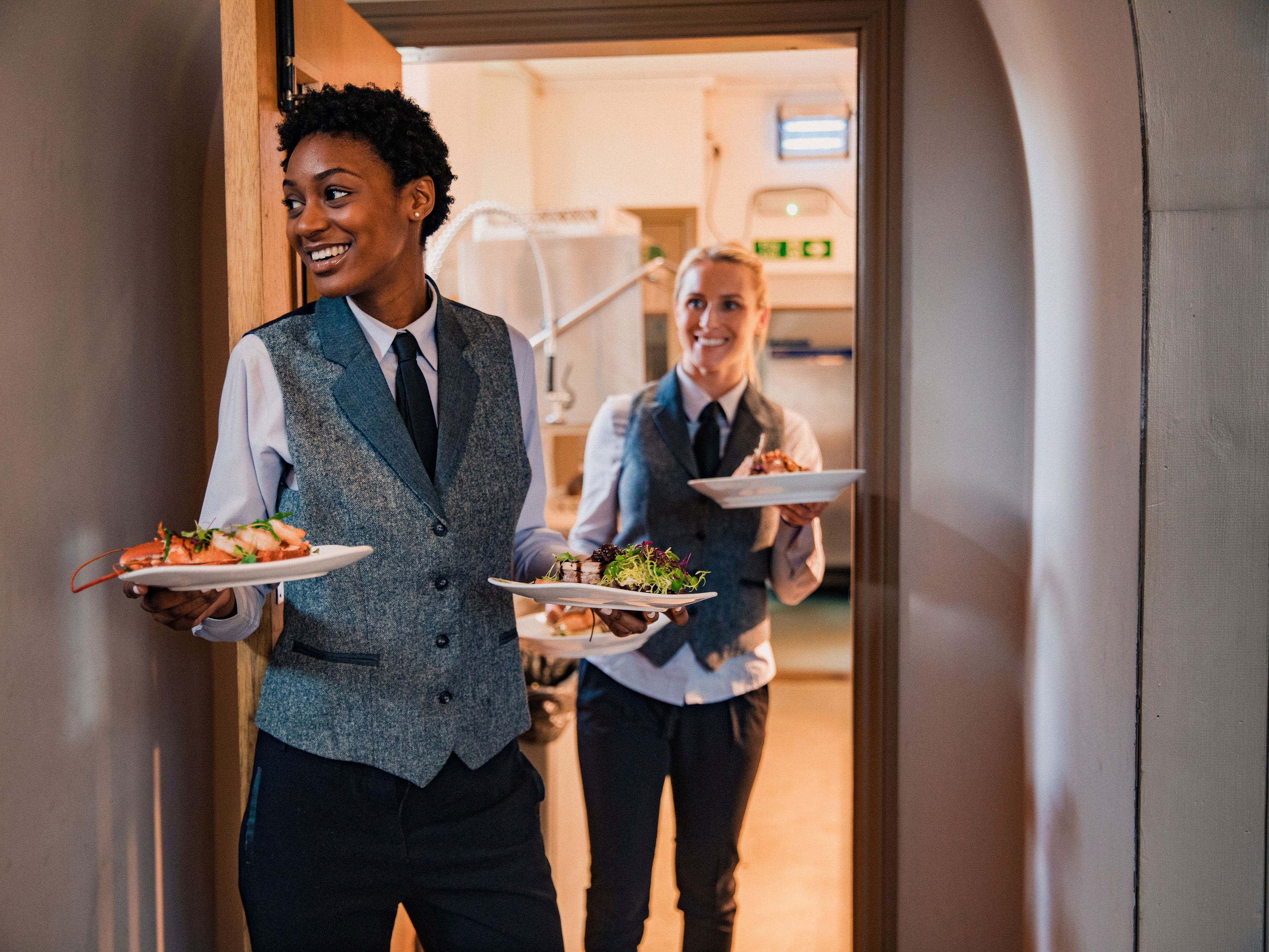 Dining servers carrying food plates from a commercial kitchen.  Dining servers carrying food plates from a commercial kitchen.