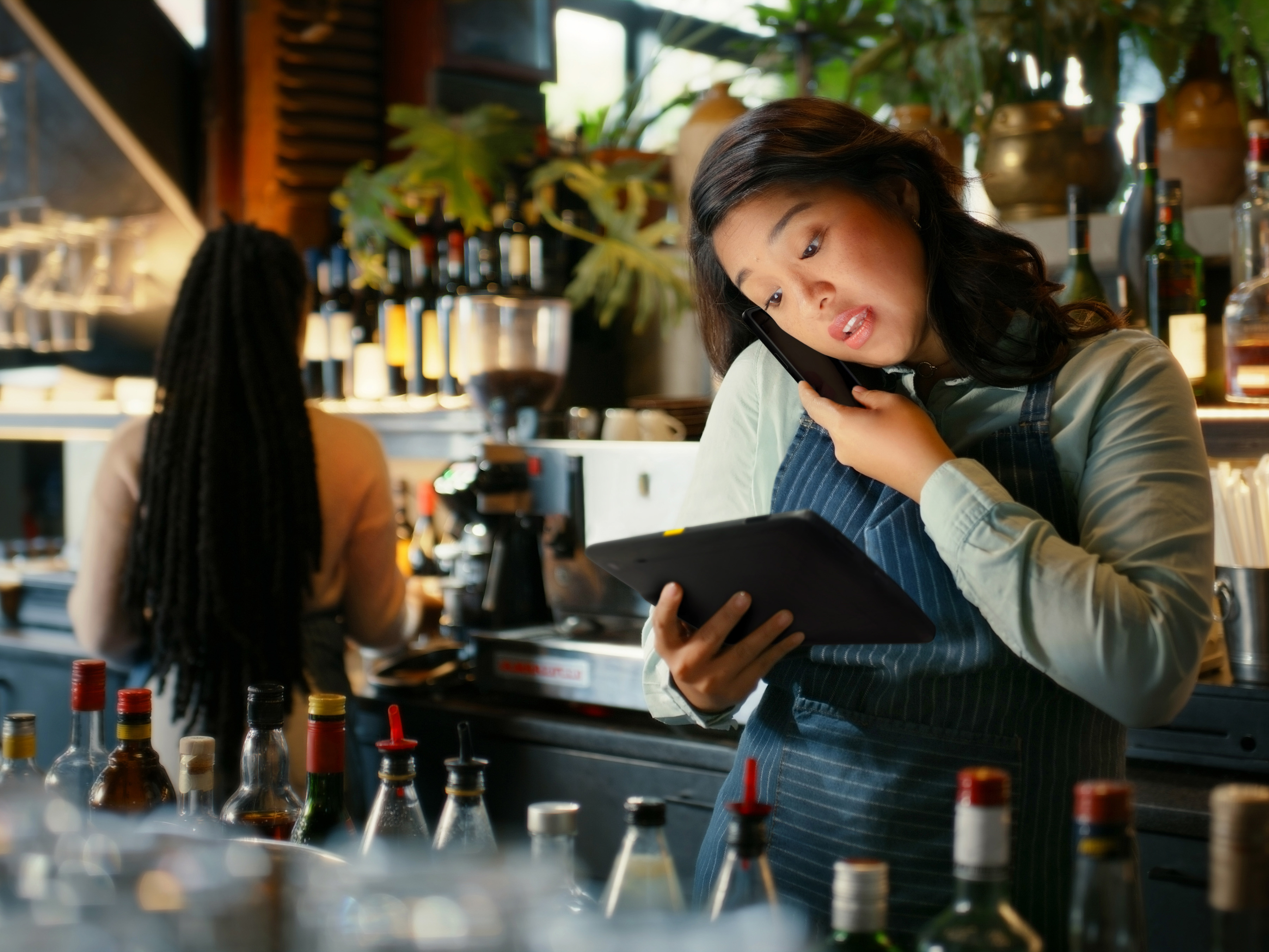 Hospitality worker using a Zebra tablet and speaking on a mobile computer behind a bar. Hospitality worker using a Zebra tablet and speaking on a mobile computer behind a bar.