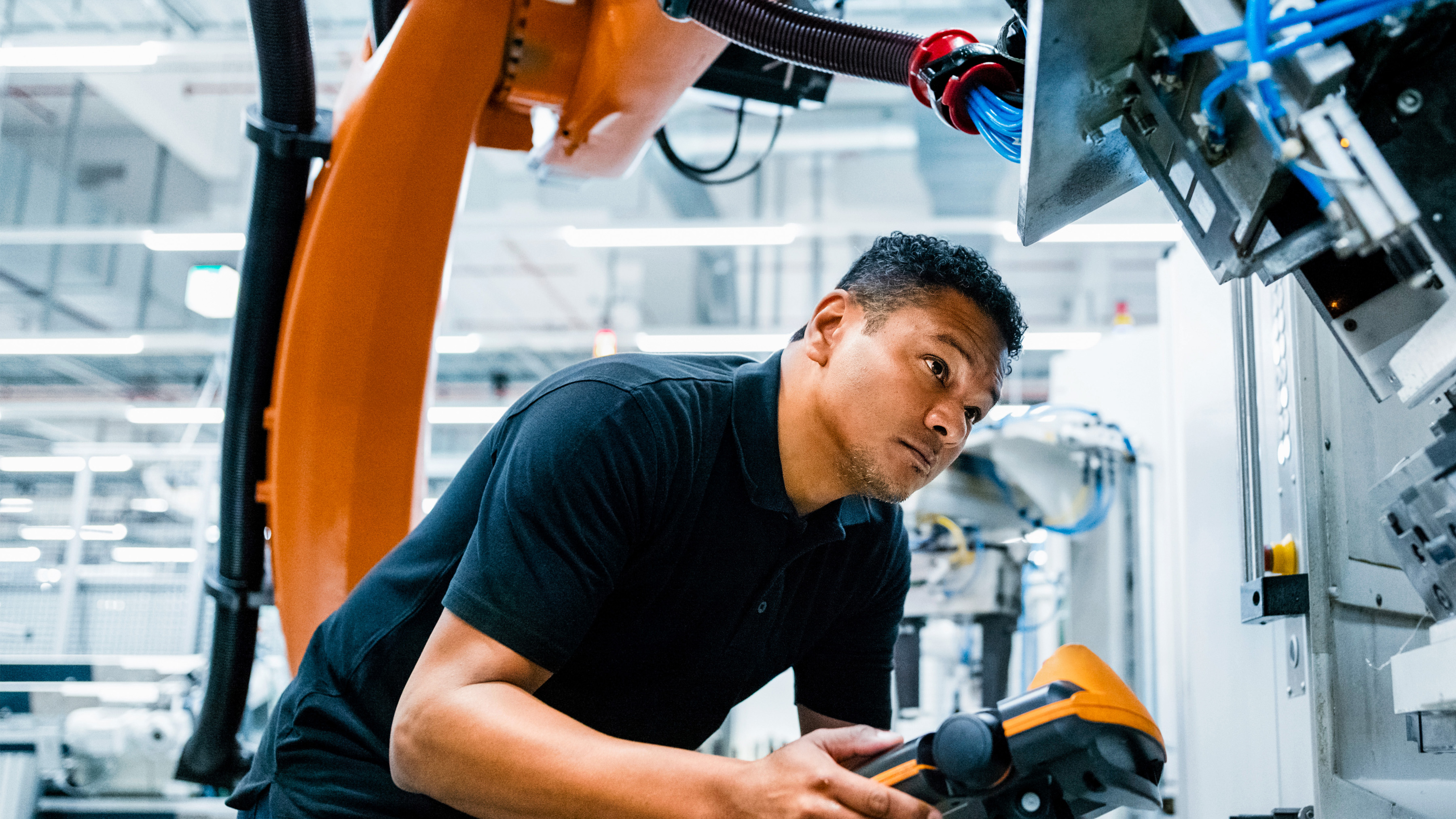 An engineer operates a robotic arm in an industrial setting using a handheld control device. An engineer operates a robotic arm in an industrial setting using a handheld control device.