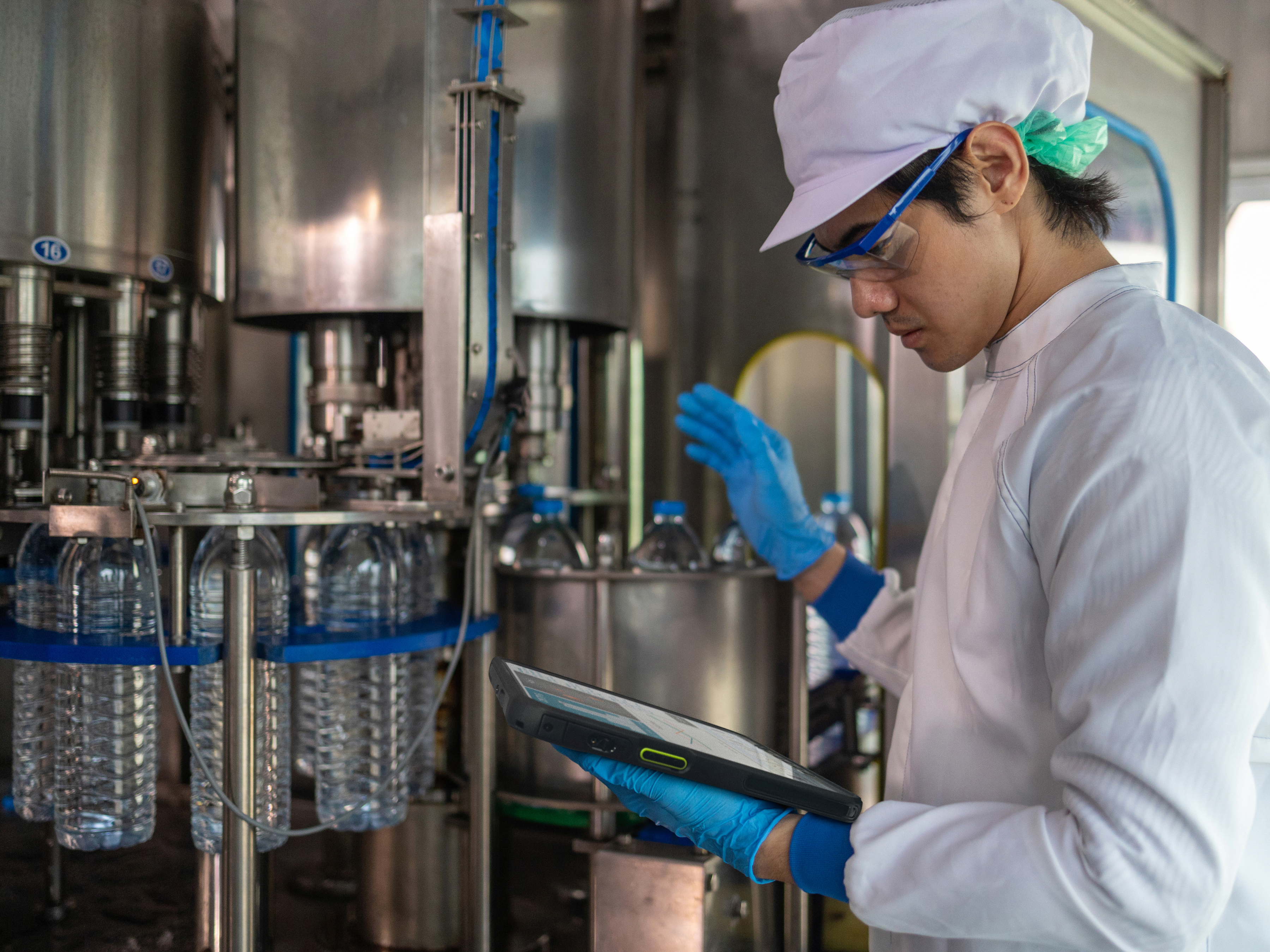 An engineer reviewing a tablet inside of a water bottle manufacturing facility. An engineer reviewing a tablet inside of a water bottle manufacturing facility.