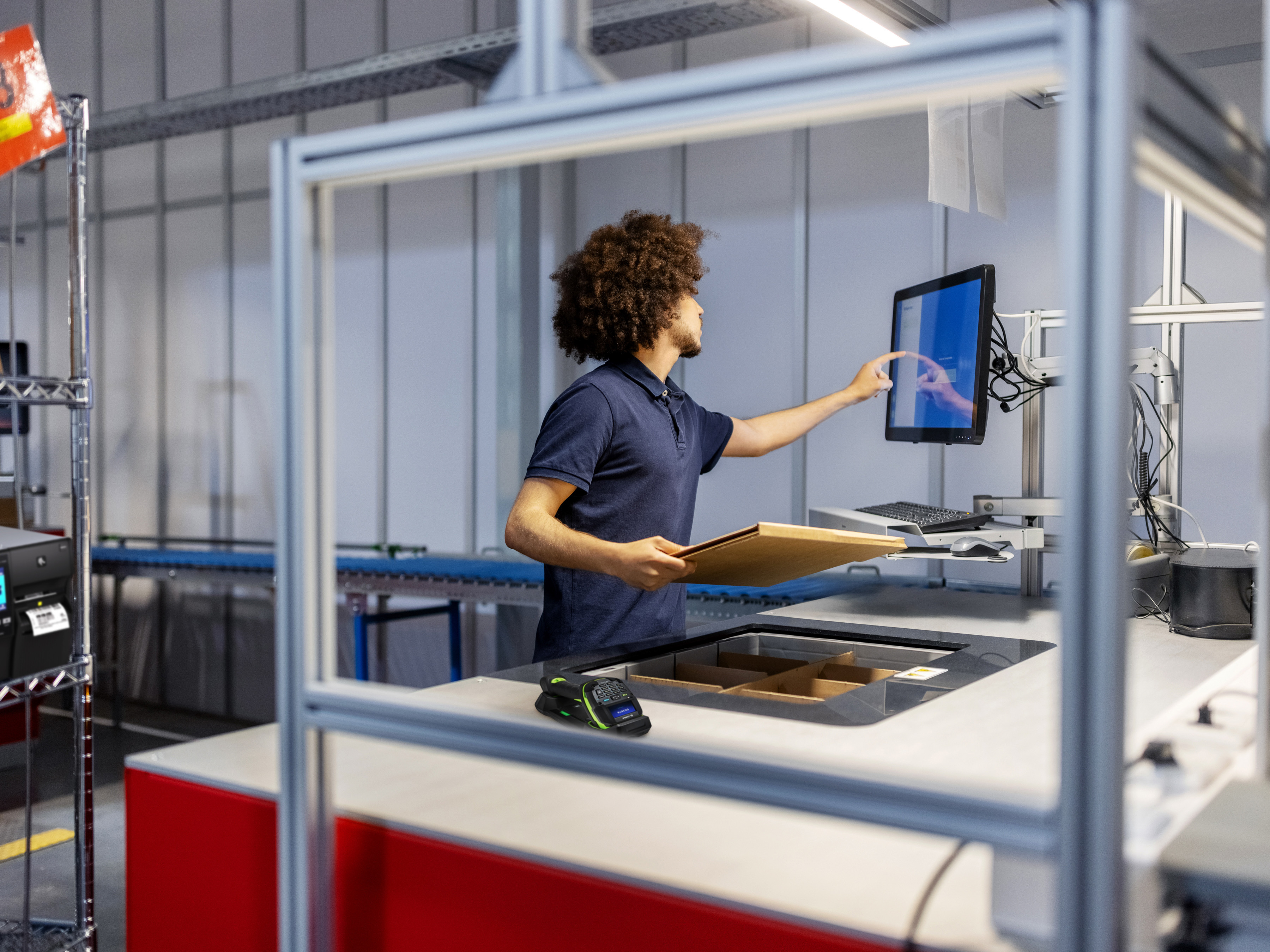 A warehouse worker processes a package on a workstation with a Zebra Industrial printer. A warehouse worker processes a package on a workstation with a Zebra Industrial printer.