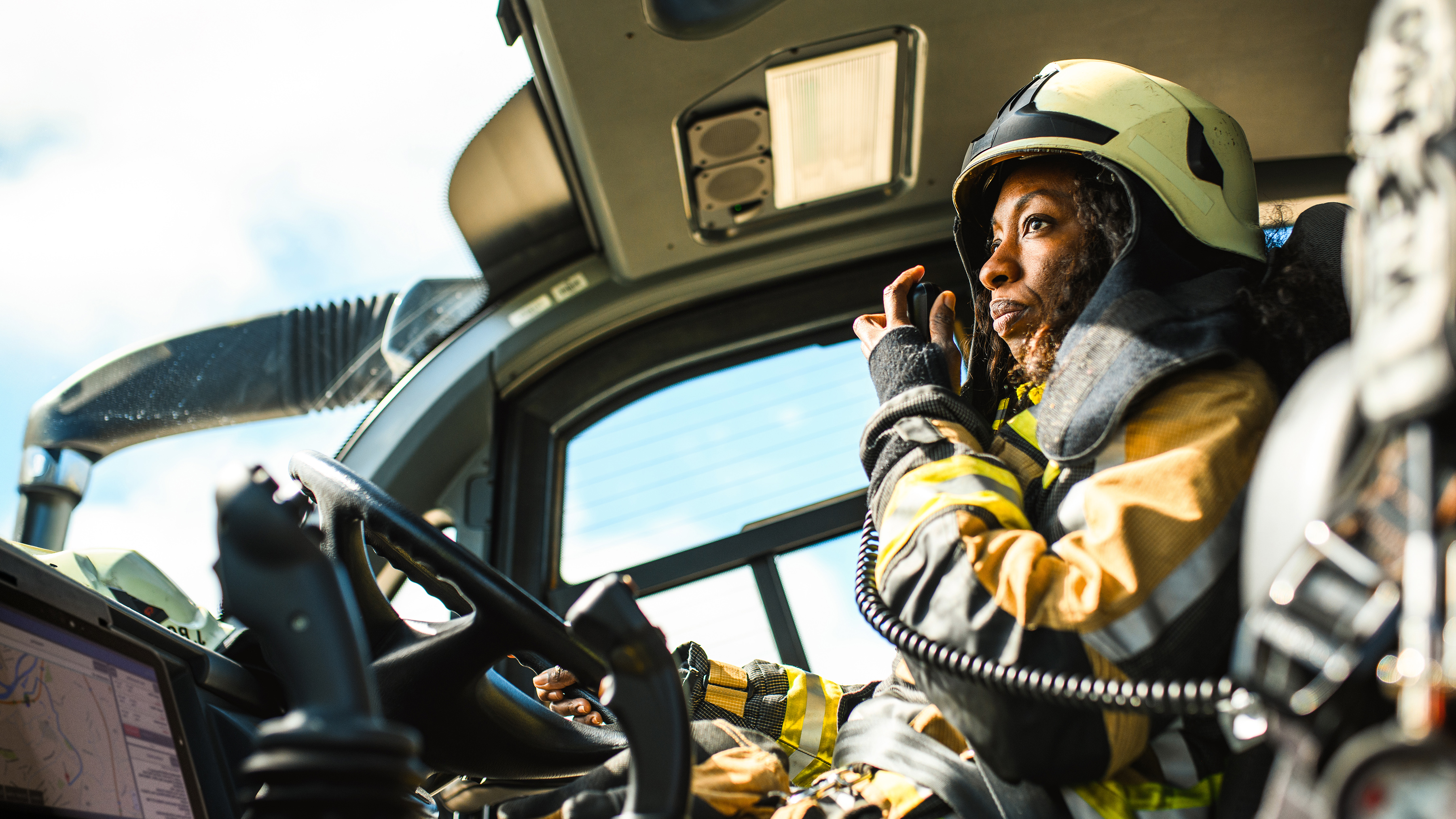 A firefighter talking on a walkie talkie with a Zebra rugged tablet while driving a firetruck. A firefighter talking on a walkie talkie with a Zebra rugged tablet while driving a firetruck.