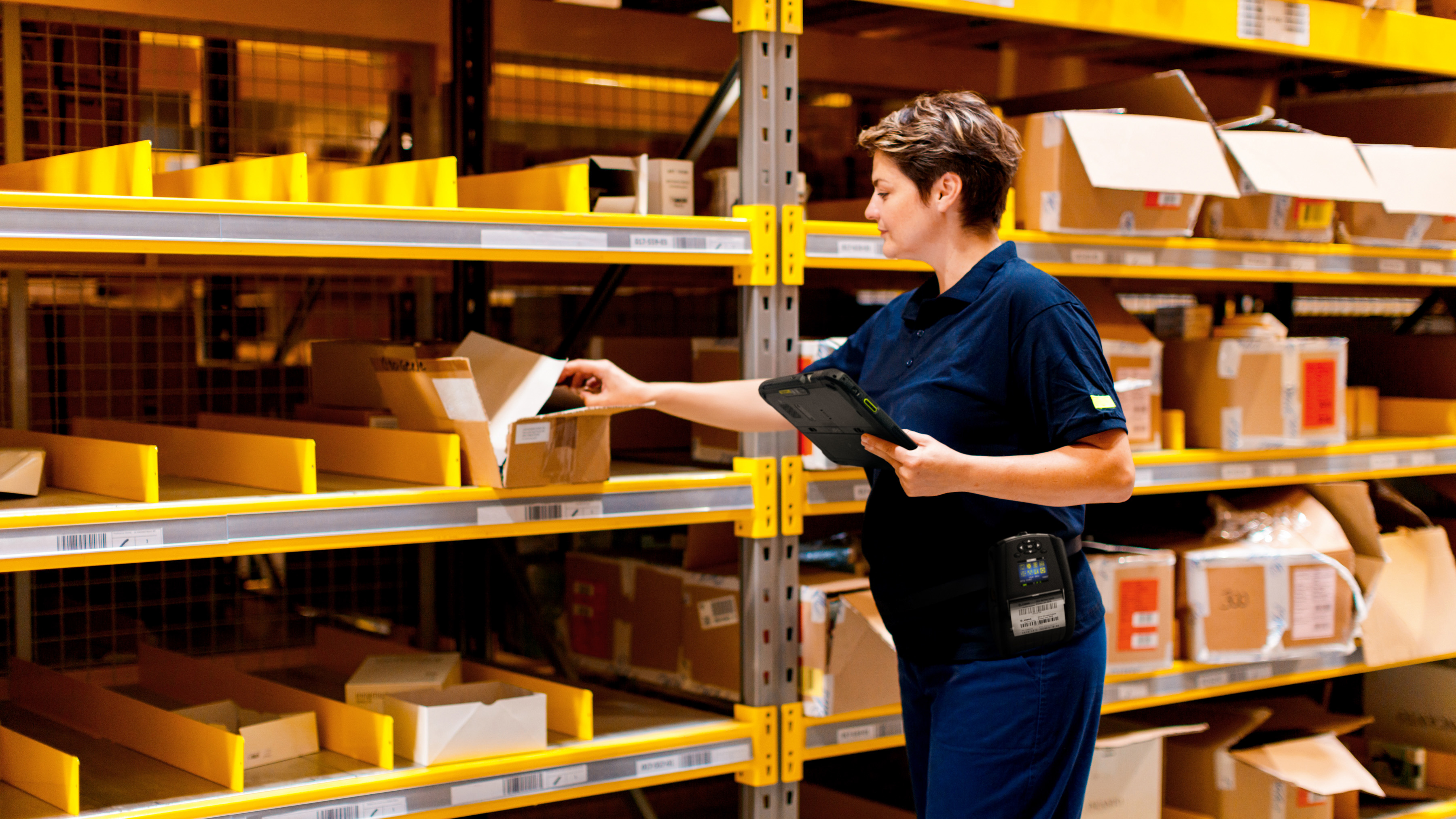 A retail worker with a Zebra tablet and mobile printer finding inventory in the store's back-of-house . A retail worker with a Zebra tablet and mobile printer finding inventory in the store's back-of-house .