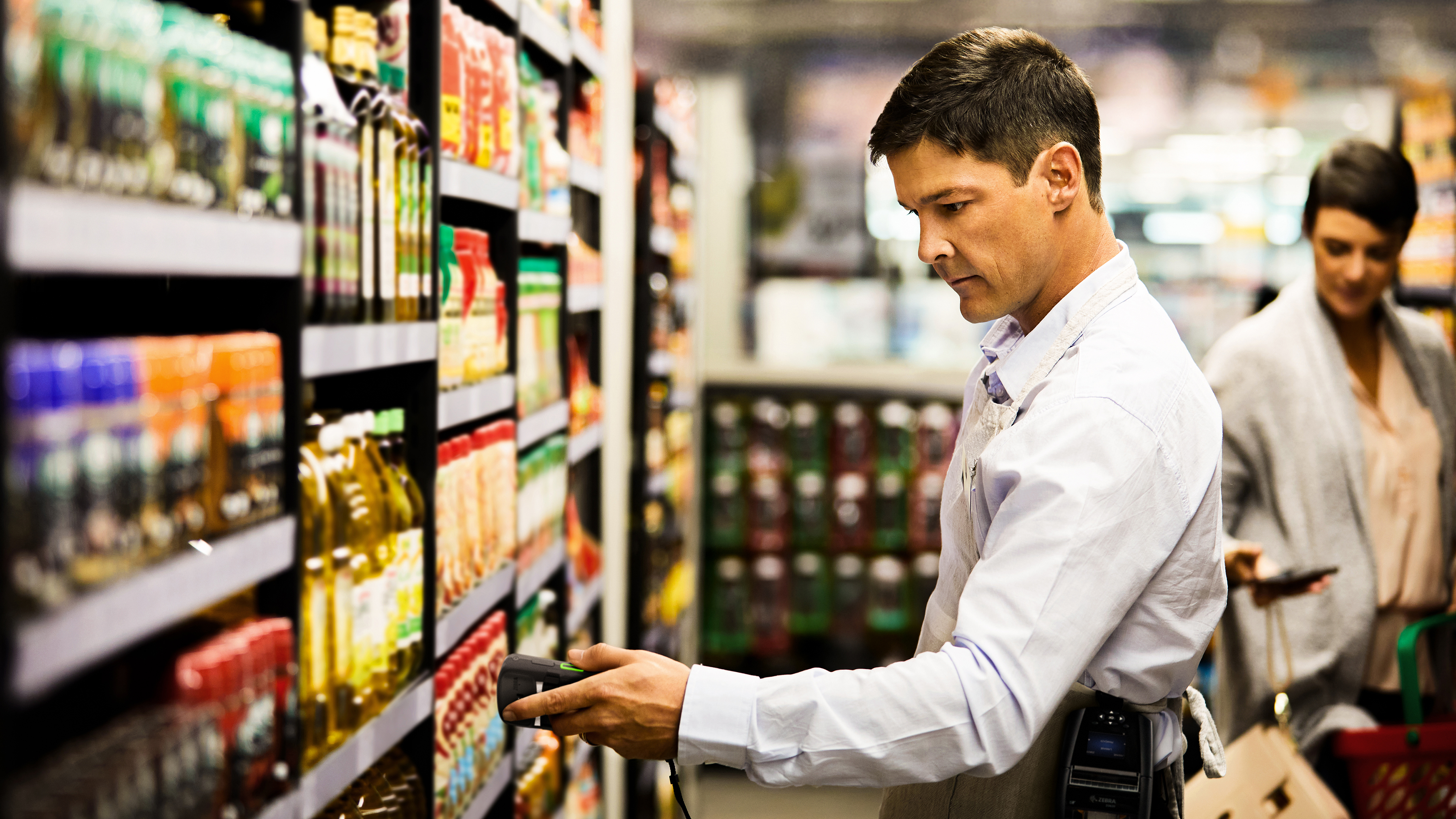 Employee scanning grocery products on shelf aisle using a tablet and handheld scanner. Employee scanning grocery products on shelf aisle using a tablet and handheld scanner.