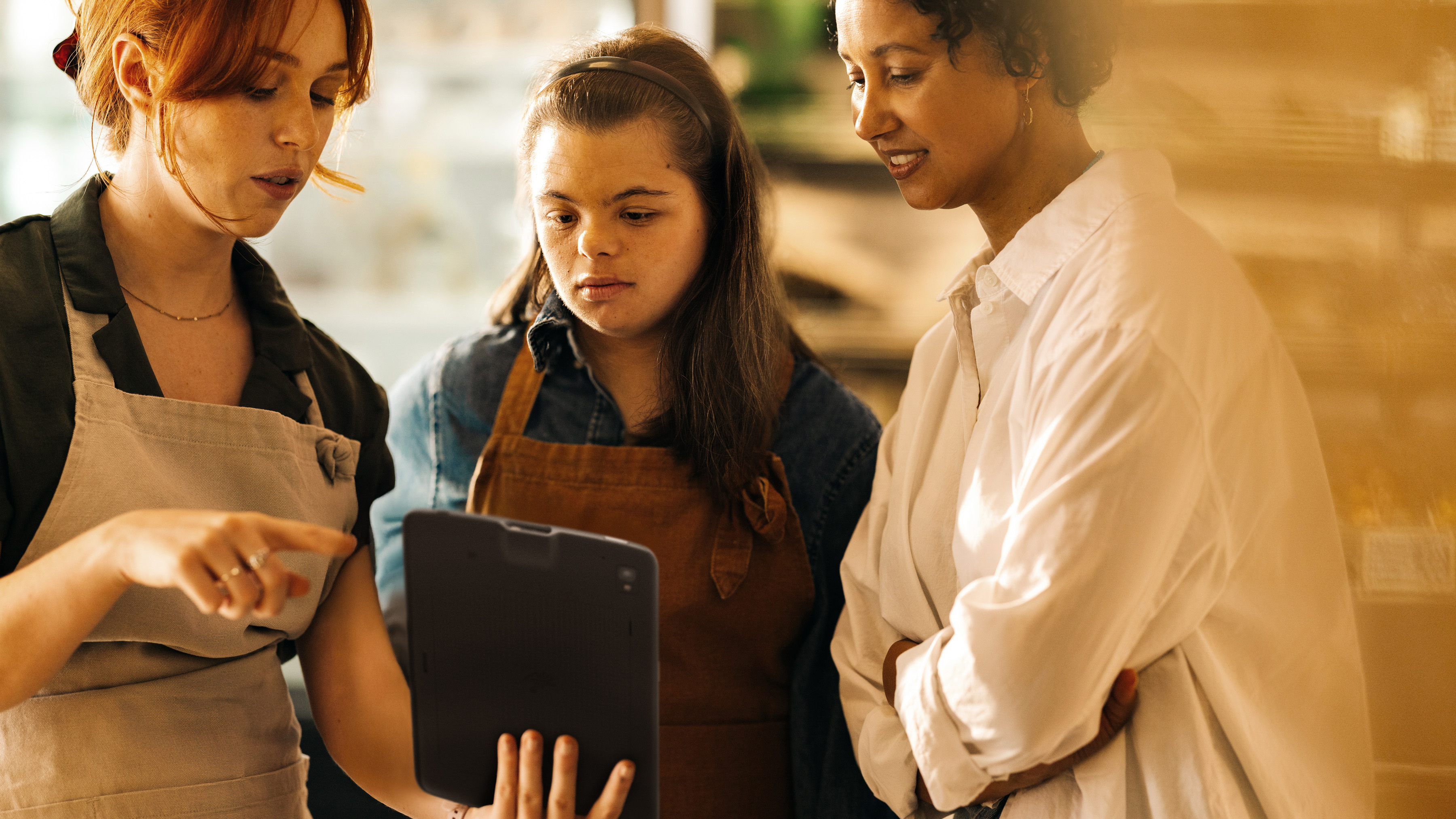 Two retail employees reviewing a tablet with a shopper inside a store's front-of-house. Two retail employees reviewing a tablet with a shopper inside a store's front-of-house.