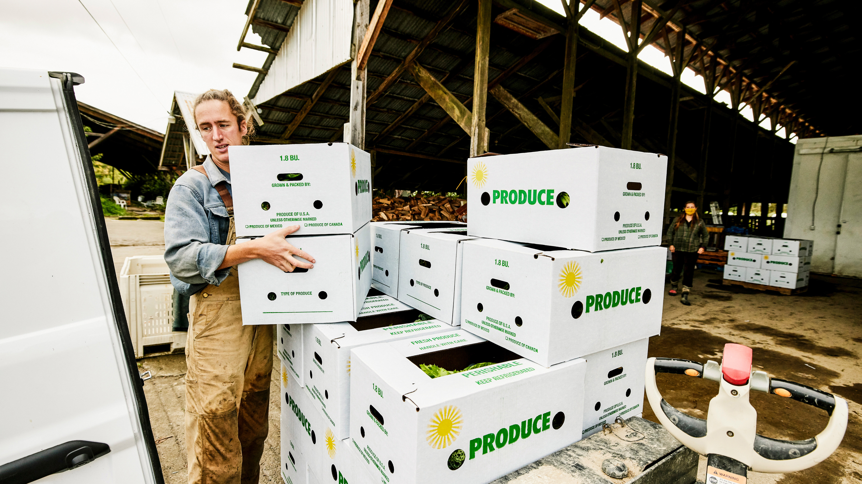 A worker is loading white boxes of produce into a vehicle near a warehouse. A worker is loading white boxes of produce into a vehicle near a warehouse.